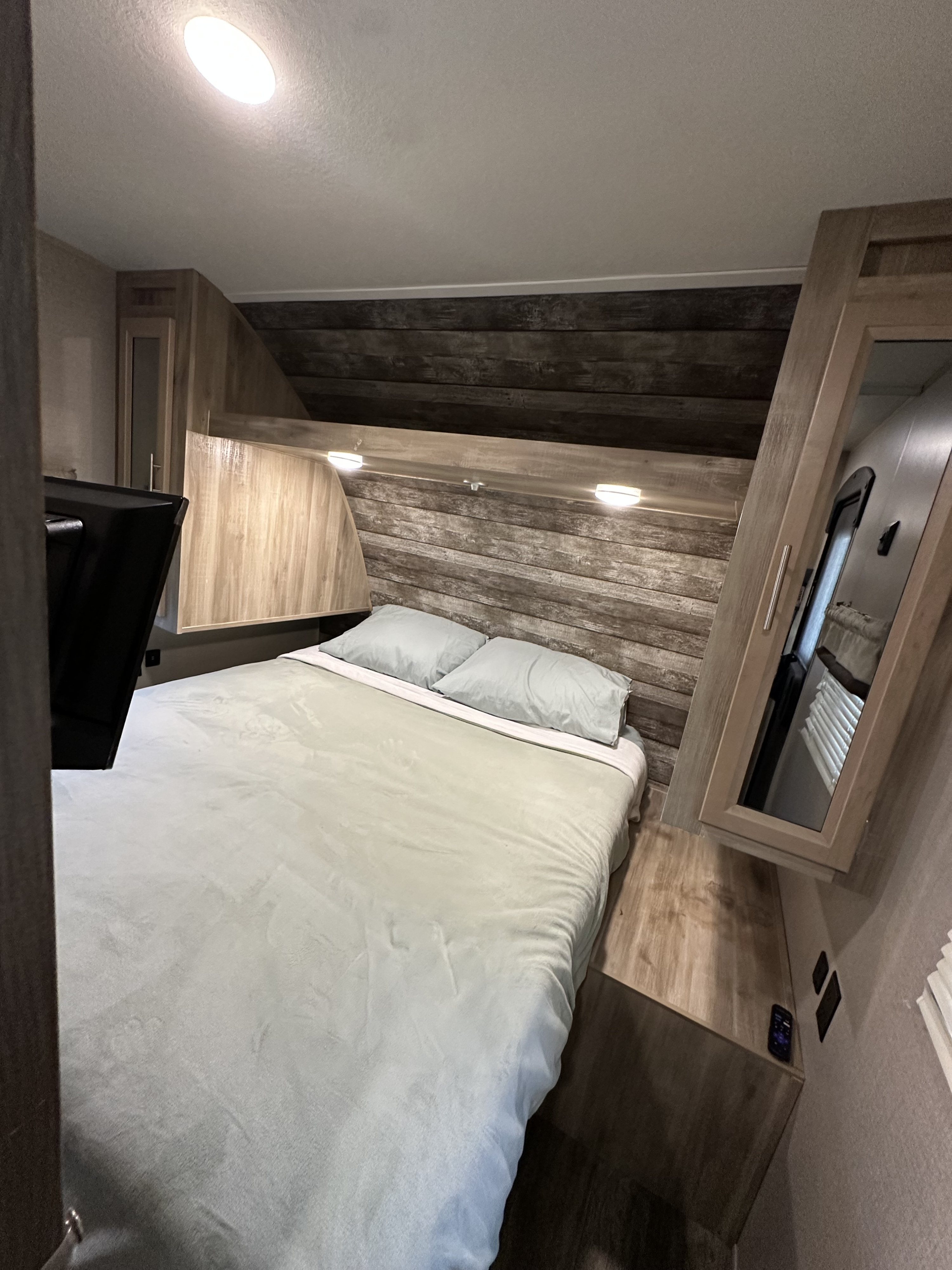 Cozy RV rental bedroom with a comfy bed, rustic wood accents, built-in storage, and a mirrored cabinet.. Coachmen Catalina Summit 261BHS 2021