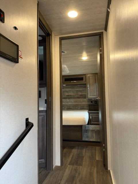 View inside an RV rental showing a hallway leading to a cozy bedroom with a comfortable bed and wood accents.. Keystone COUGAR HALF TON 2023