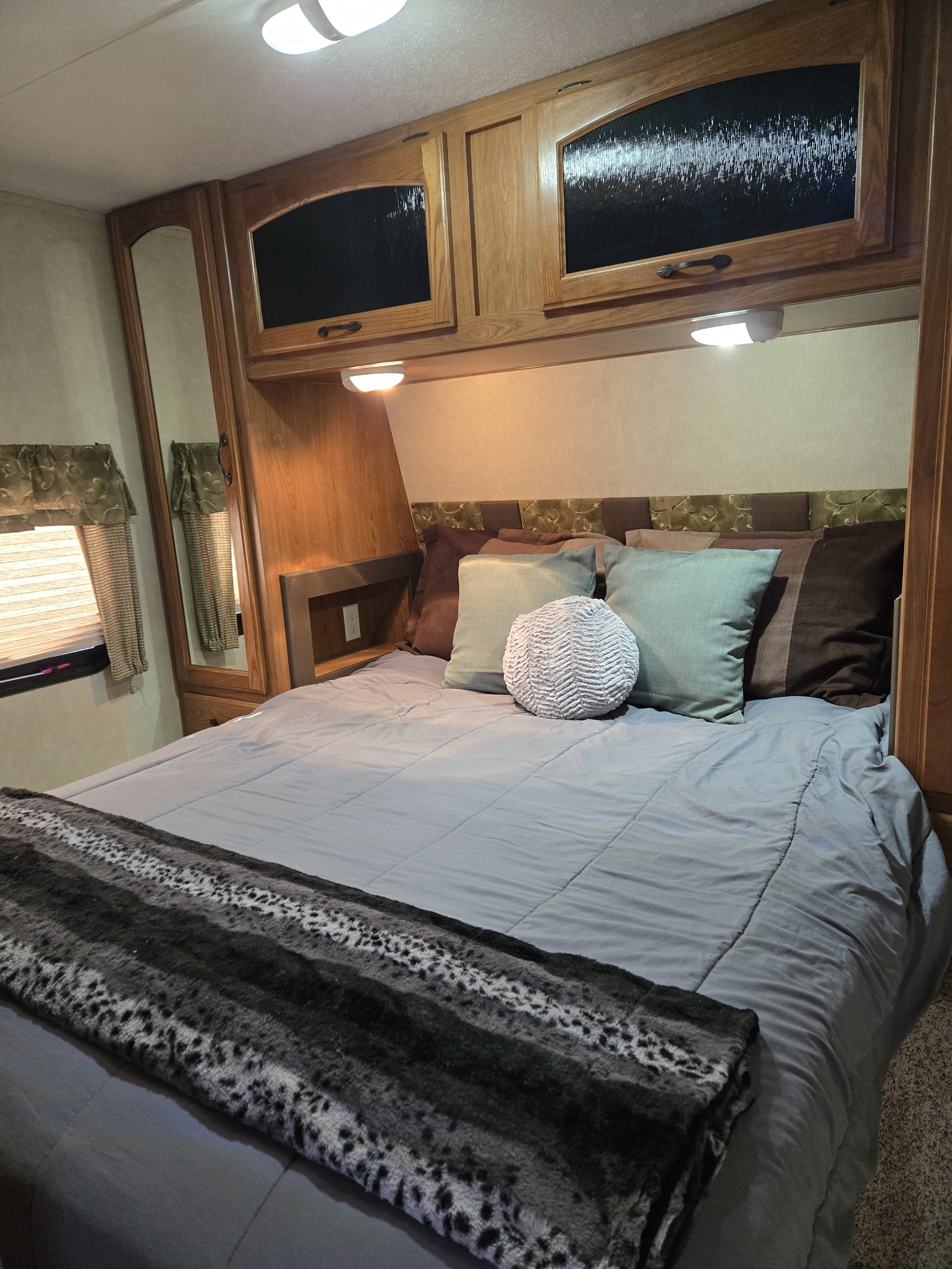 Cozy RV rental bedroom featuring a comfortable bed with soft linens, overhead storage, and reading lights, ideal for travel.. Keystone RV Sprinter 2012