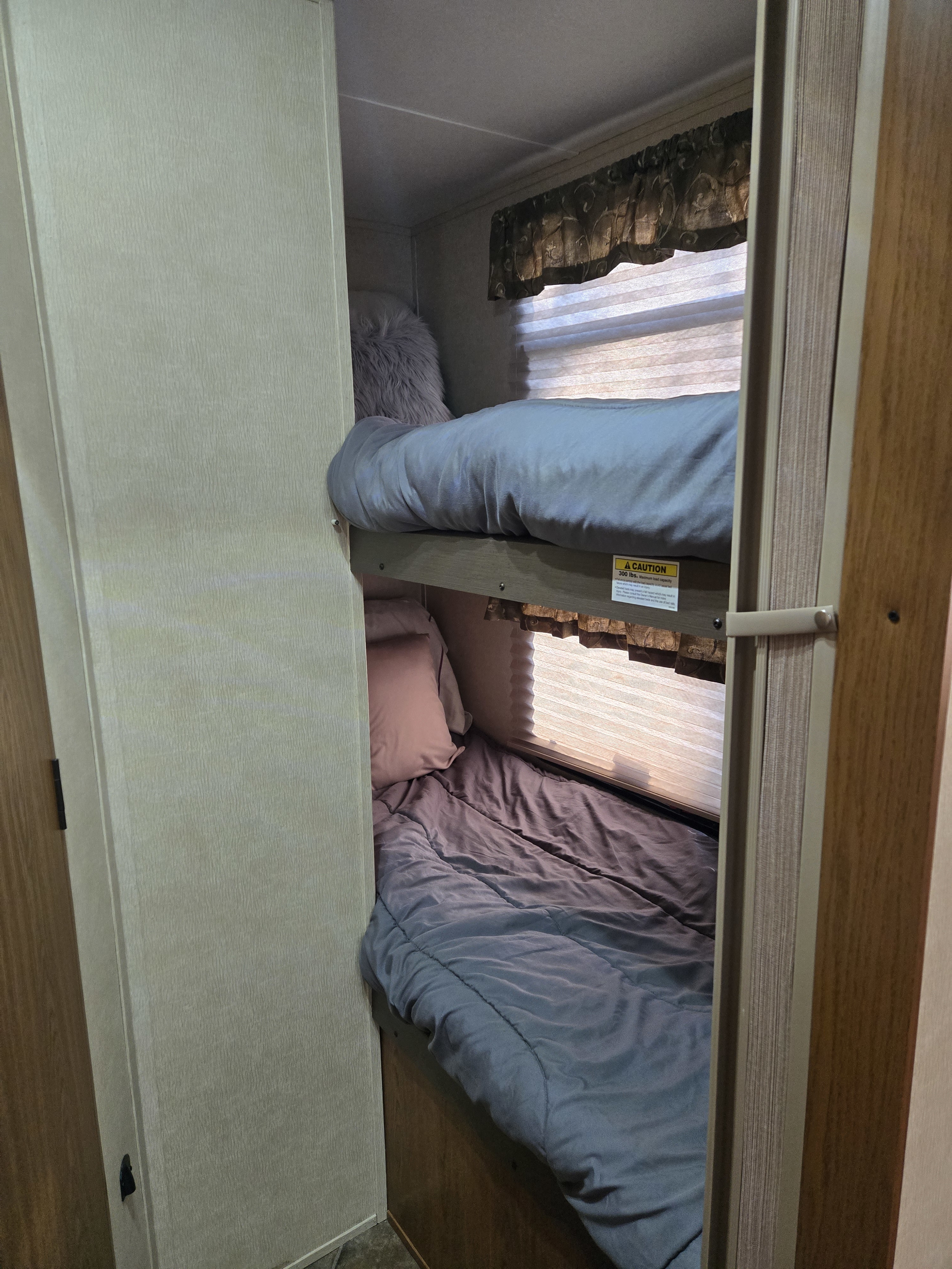 Inside an RV rental: two stacked bunk beds. Top bunk has light blue bedding; bottom has dark gray. Ideal for compact sleeping.. Keystone RV Sprinter 2012