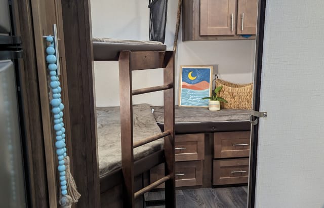 RV rental bunk beds: a cozy interior with a ladder, decorative art, plant, and storage drawers for a comfortable stay.. Forest River Wildcat Ultra Lite 2019