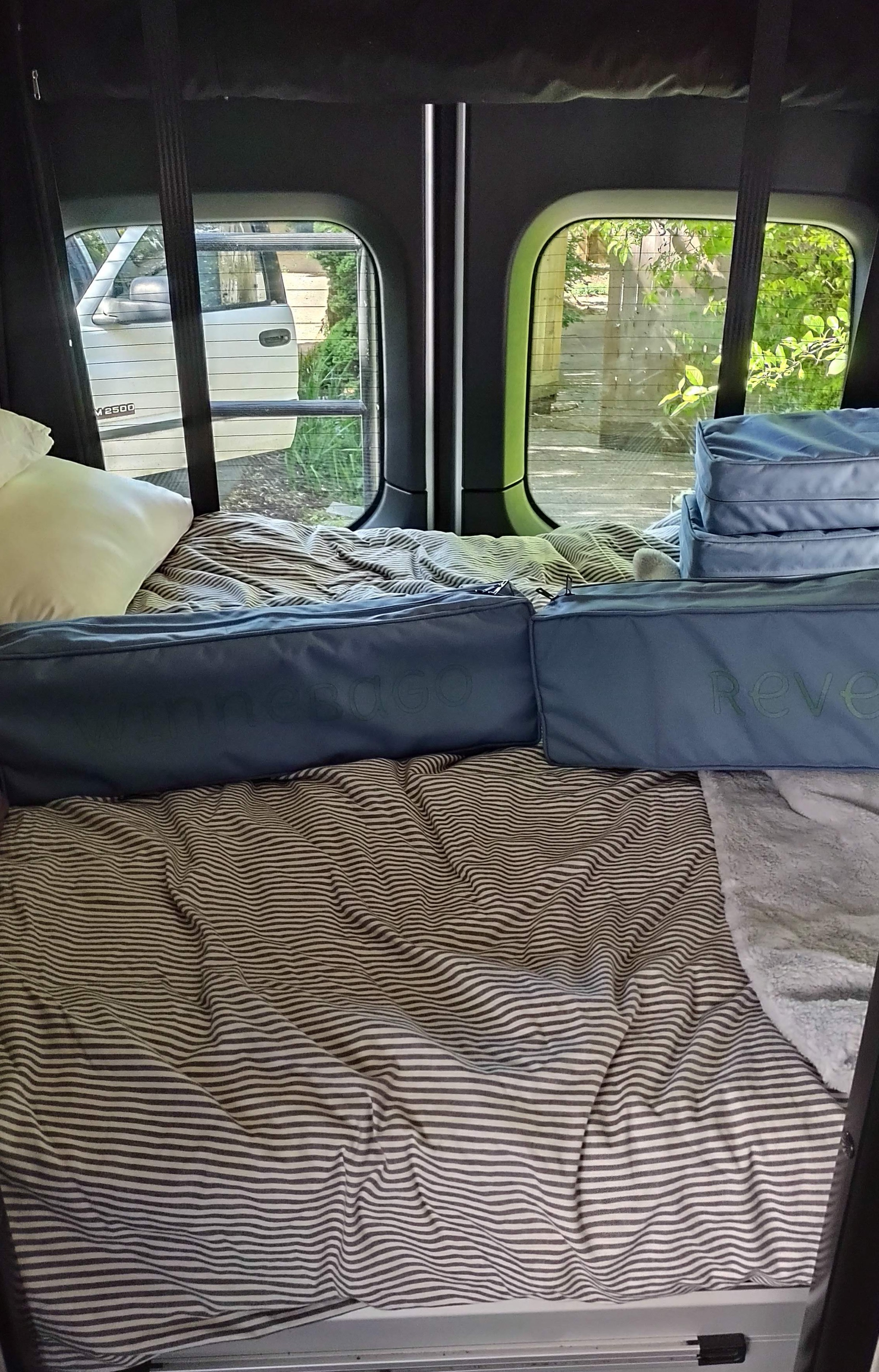 Revel RV rental interior: striped bed, pillow, and Omnesdo storage bags for a comfy journey.. Winnebago Revel 2021