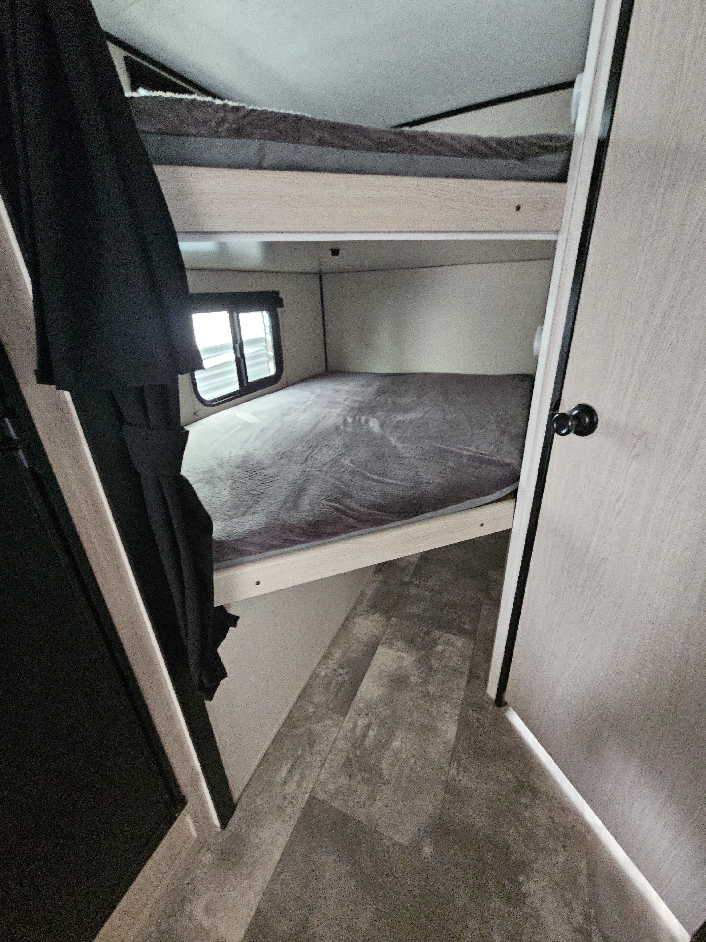Cozy RV rental bunk beds: an upper and lower bunk with grey bedding, window, and wood paneling, seen from an entryway.. Coachmen Apex Nano 2022