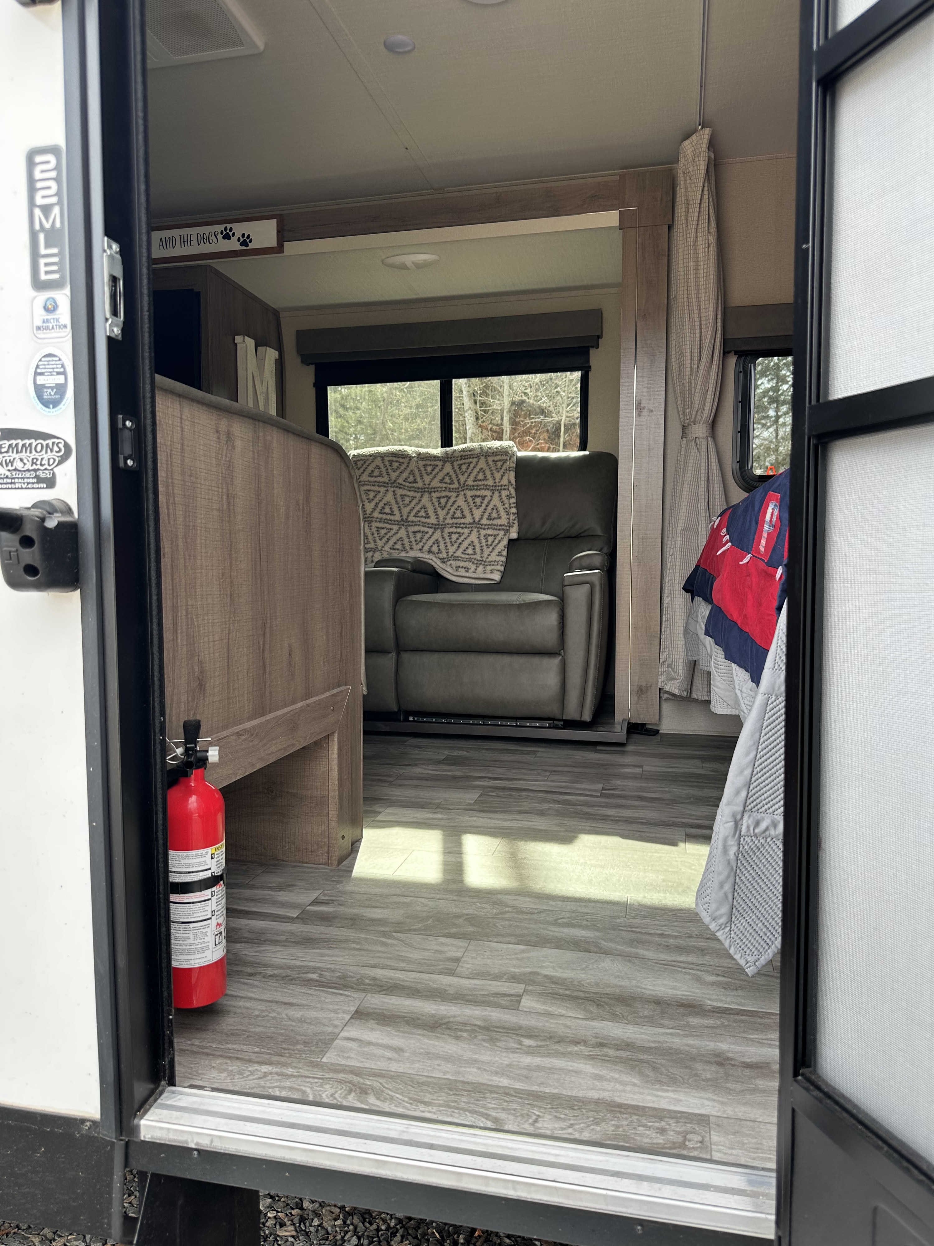 Step into this cozy RV rental, featuring a living area with a recliner, wood-look flooring, and a fire extinguisher.. Grand Design Imagine XLS 2022