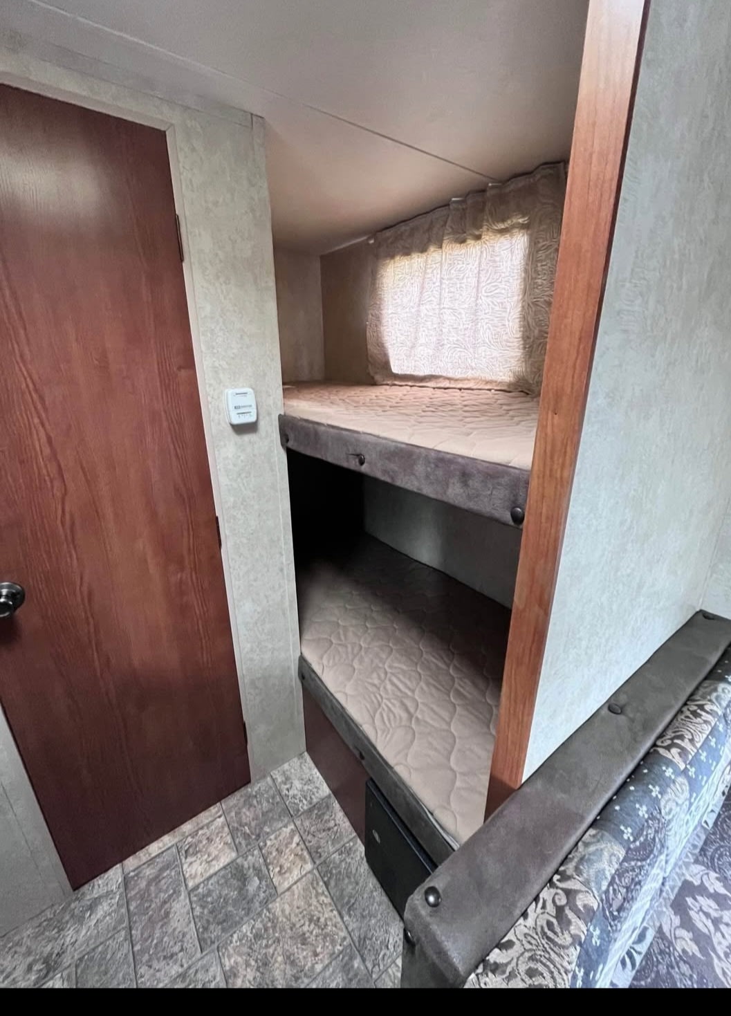 This RV rental features a cozy sleeping area with two bunk beds (mattresses visible), a brown door, and patterned sofa. Ideal camper.. Forest River Salem Cruise Lite 2013