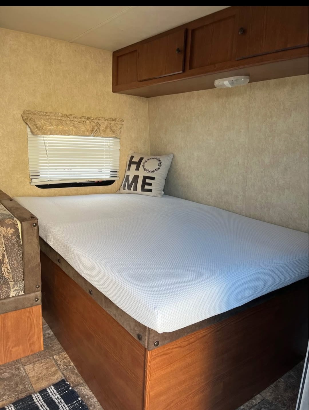 Relaxing RV rental sleeping area featuring a bed with a 'HOME' pillow, window, and ample wooden storage.. Forest River Salem Cruise Lite 2013