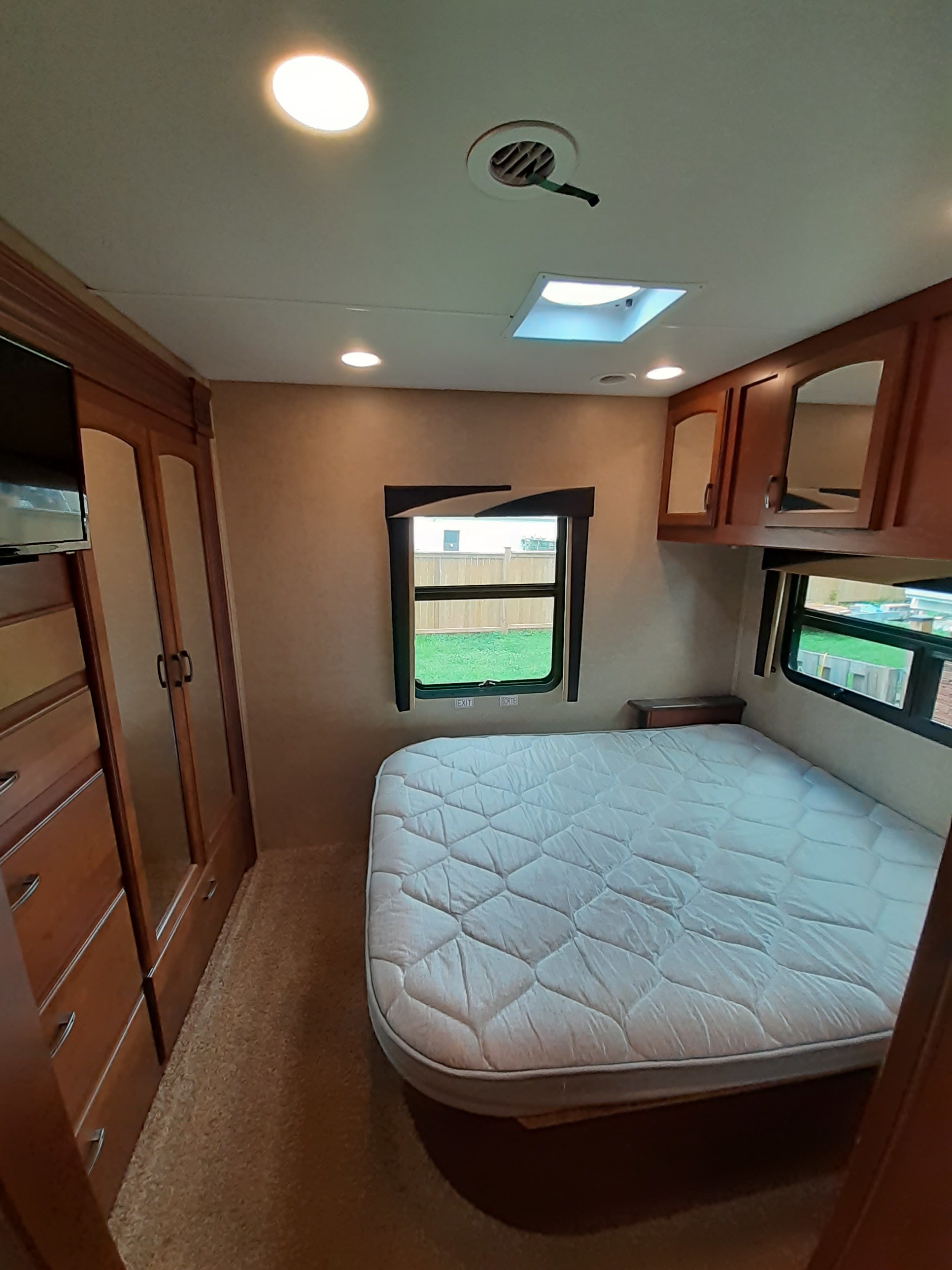 RV rental: Bright bedroom with quilted mattress, wood cabinetry, recessed ceiling lights, and windows showing a fence and grass.. Jayco Greyhawk 2015