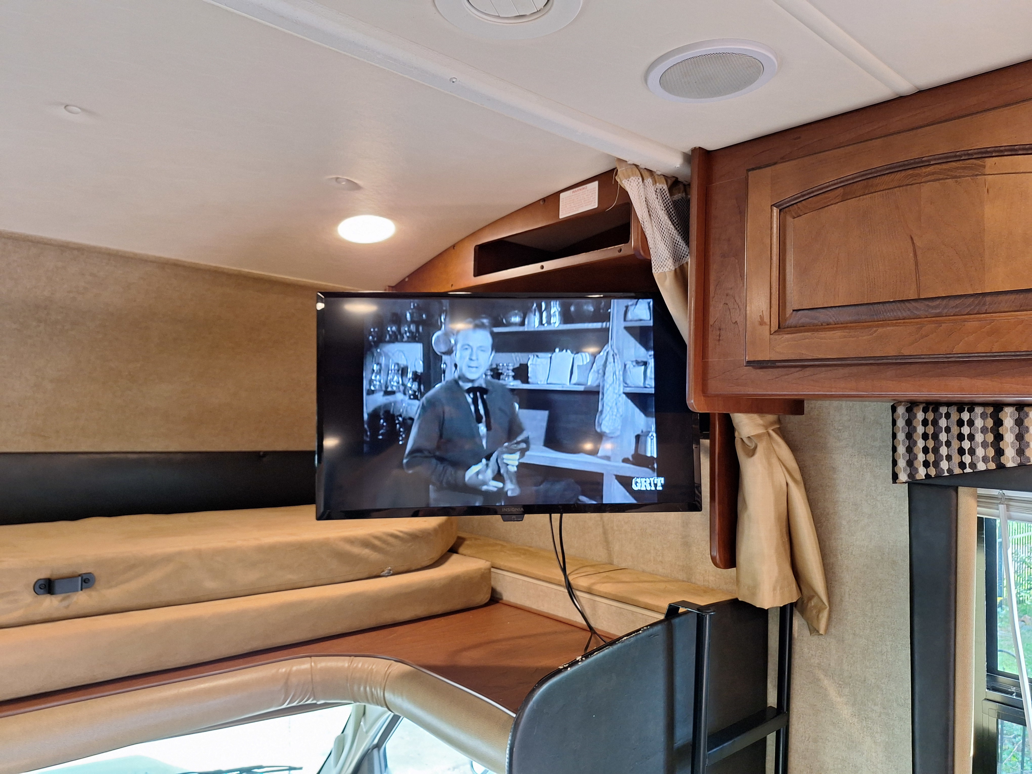 Cozy RV rental interior: TV playing a classic movie above comfortable bunk beds, ideal for travel and relaxation.. Jayco Greyhawk 2015