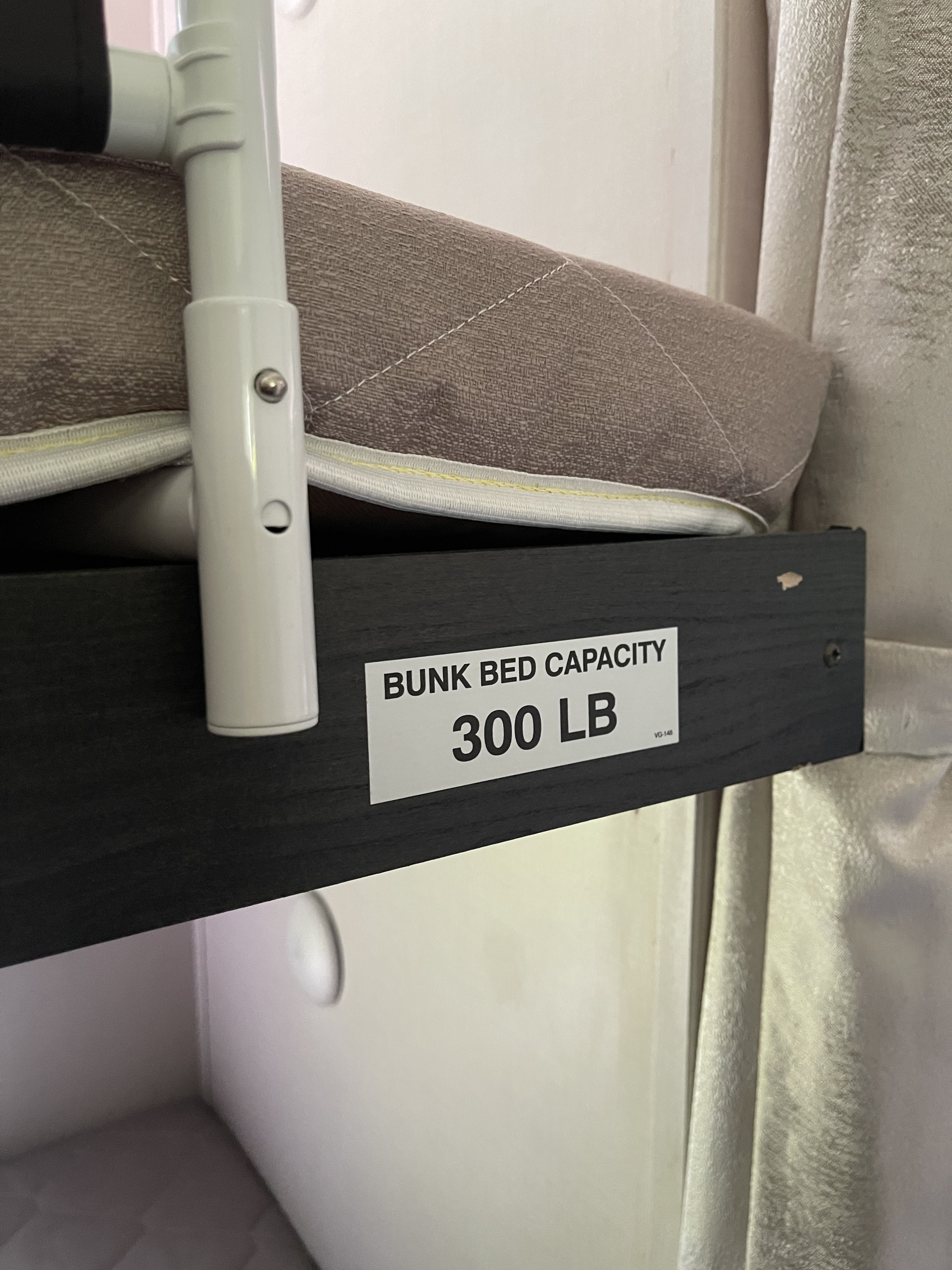 RV rental bunk bed with a "300 LB" capacity sticker on its dark frame, featuring a mattress and white support pole.. Forest River Surveyor Legend 2019