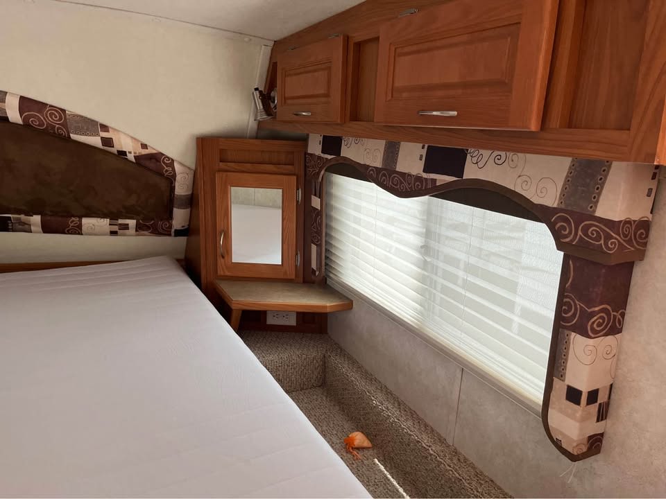 RV rental bedroom interior featuring a bed, wood cabinets, mirror, window with valance, and carpeted steps.. Kodiak Kodiak Fifth Wheel 2006