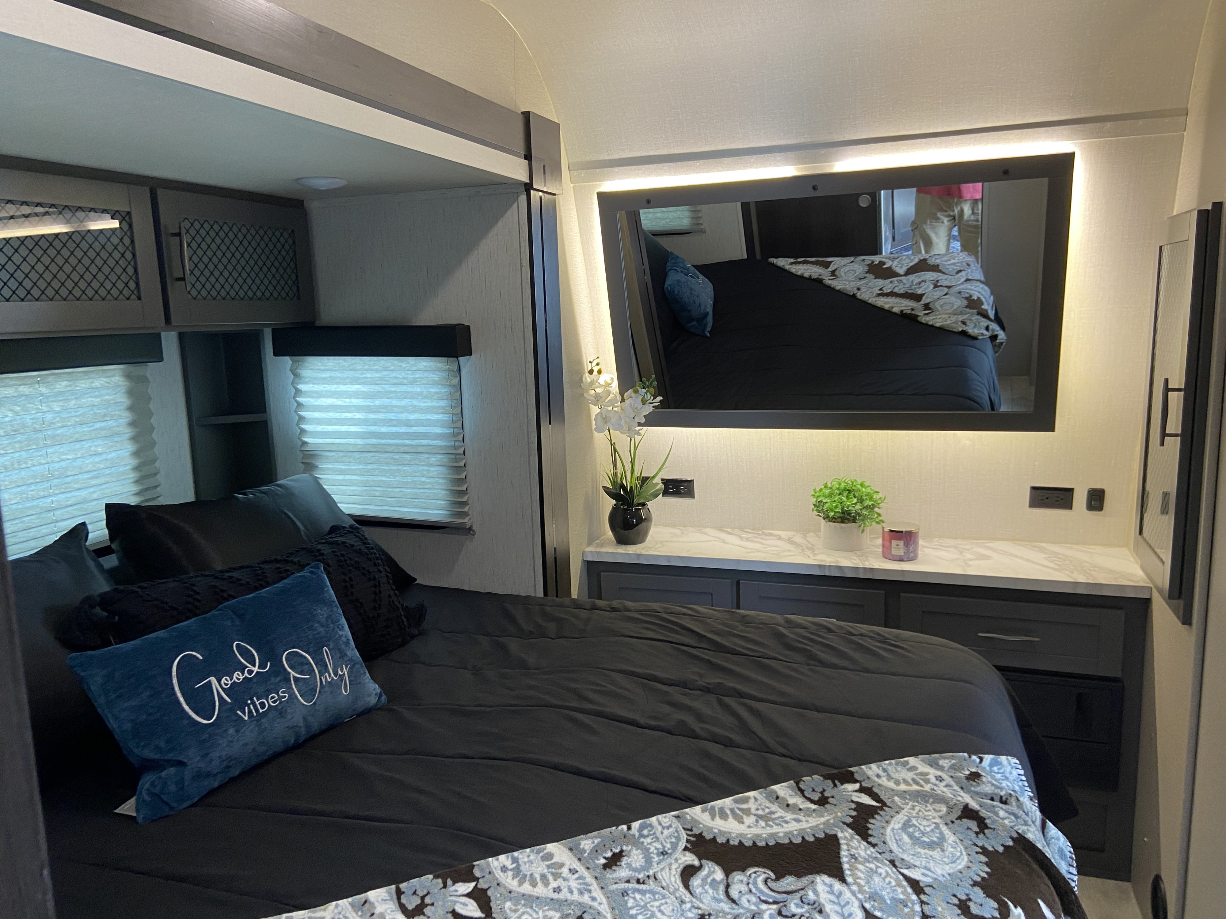 Cozy RV rental bedroom with modern decor, comfortable black bedding, vanity, and overhead storage for your road trip.. Grand Design Momentum 2022