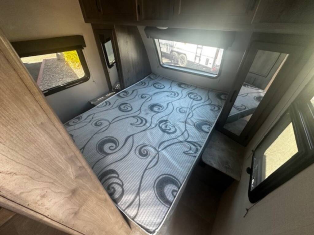 Step inside this RV rental's bedroom: a compact space with a patterned mattress, windows, and overhead cabinets.. Coachmen Apex 2021