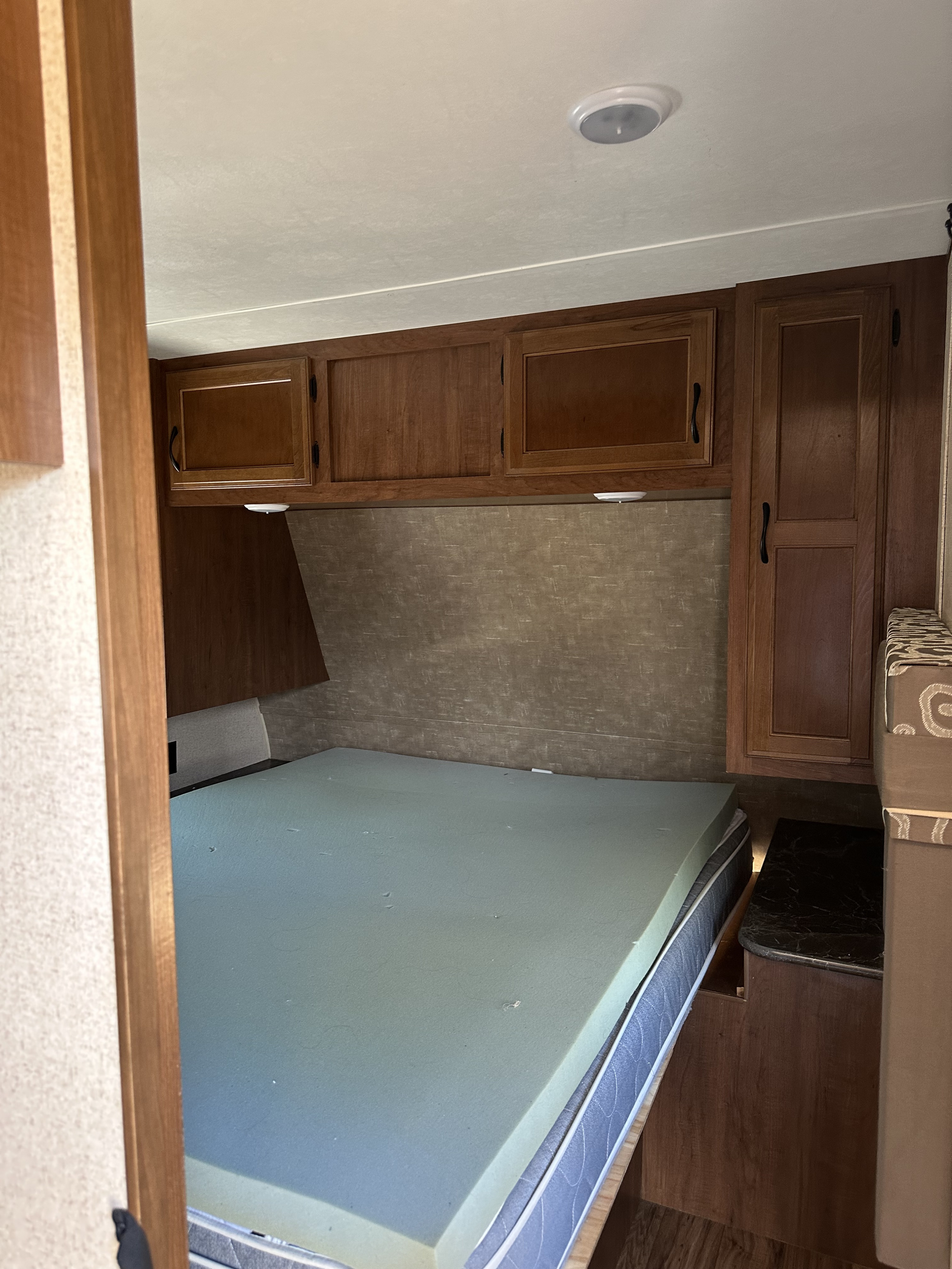 RV rental interior: a compact bedroom with a bed, light green topper, overhead wood cabinets, and integrated storage.. Jayco Jay Flight 2016