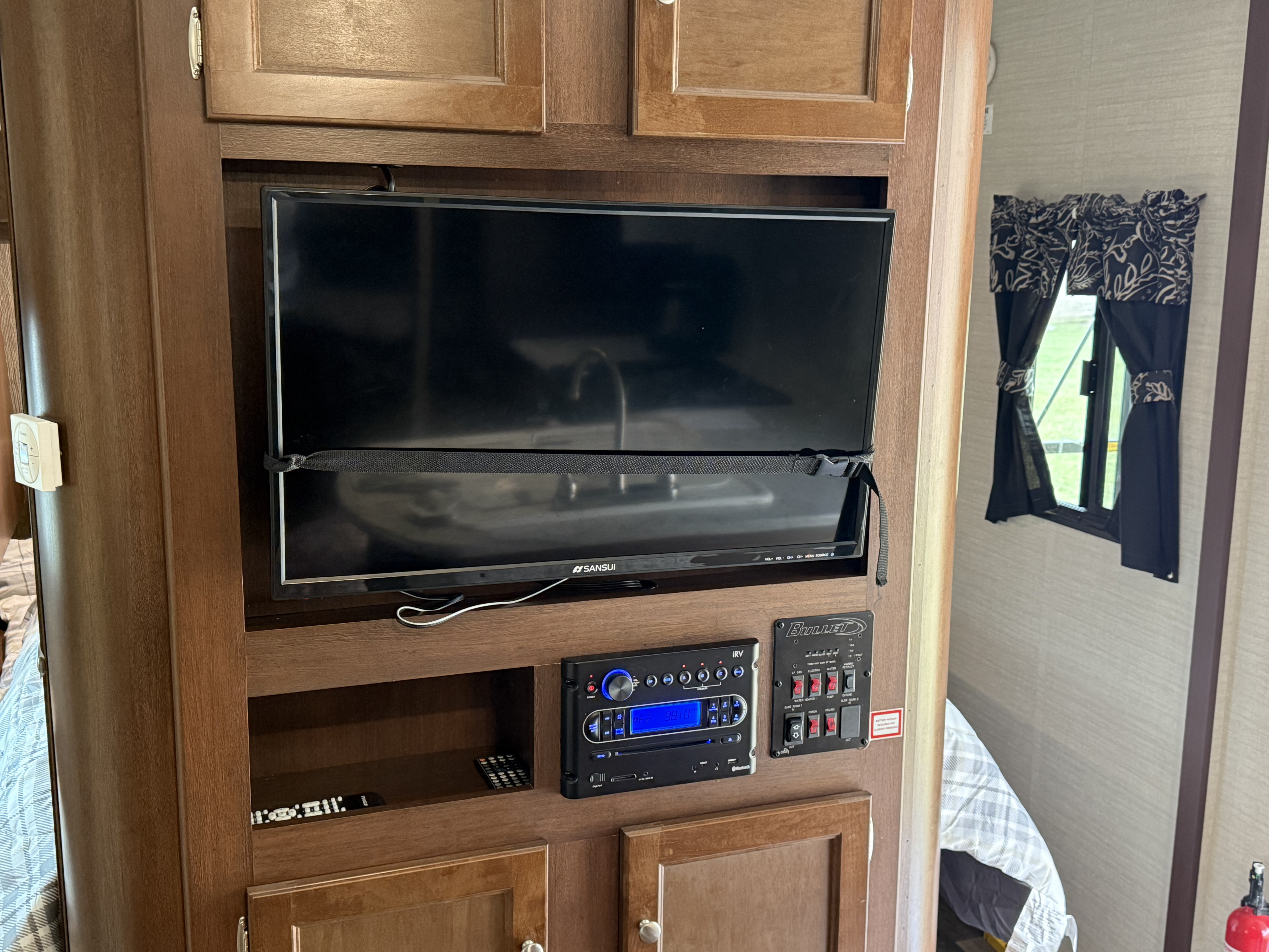 Inside an RV rental, showing the entertainment setup with a secured TV, stereo, and RV control panel built into the wooden cabinetry.. Keystone RV Bullet Ultra Lite 2017