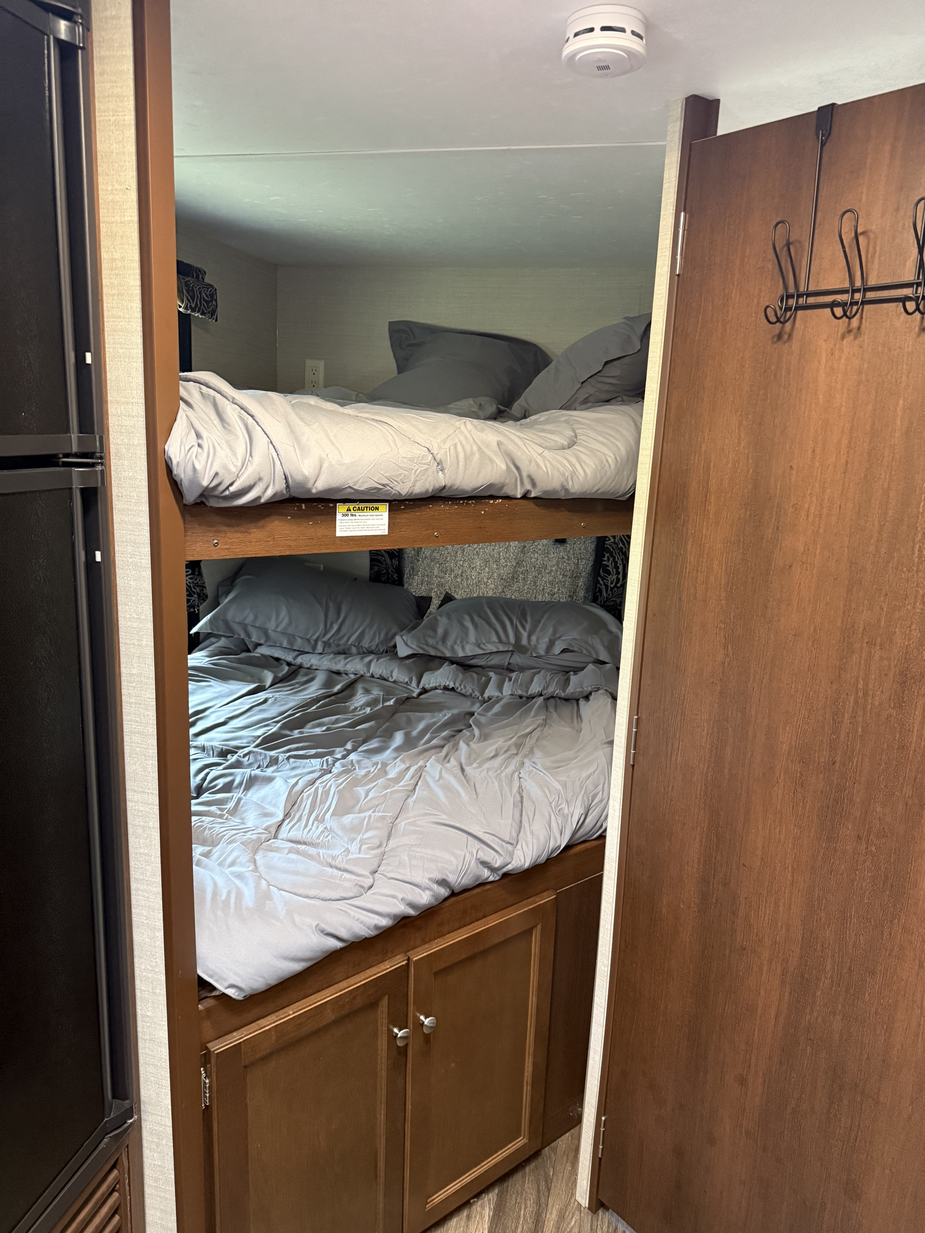 Cozy bunk beds with grey bedding in an RV rental, featuring a fridge, closet hooks, and a 300 lbs top bunk limit.. Keystone RV Bullet Ultra Lite 2017