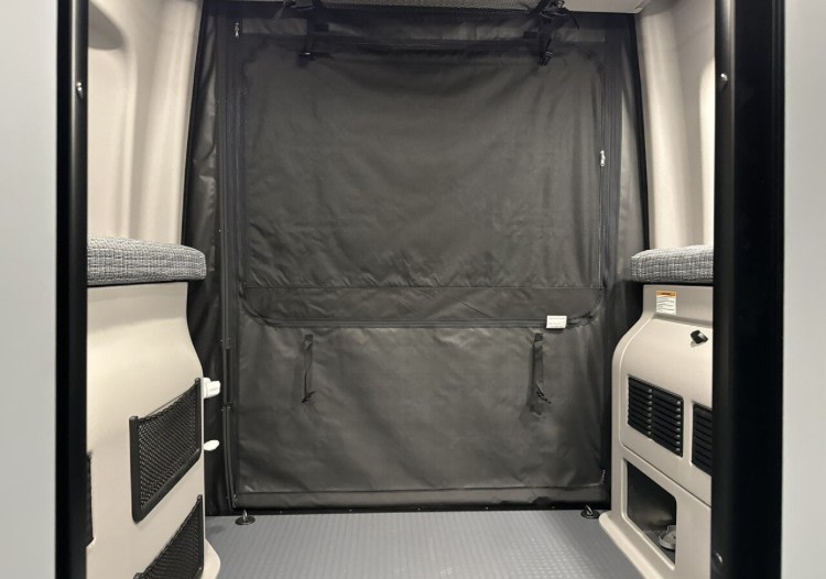 RV rental interior looking to the rear. Black privacy curtain, side benches with storage, and grey floor.. Winnebago Revel 2024