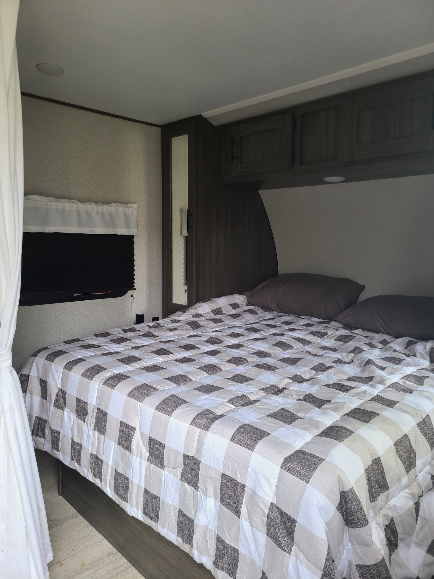 Cozy RV rental bedroom featuring a plaid comforter, dark pillows, and storage cabinets. A comfortable RV interior.. Forest River Shasta 2021