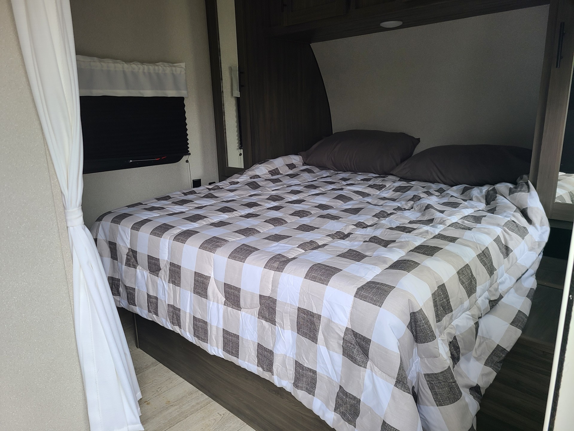 Cozy RV rental bedroom with a plaid comforter, built-in storage, and dark wood accents.. Forest River Shasta 2021