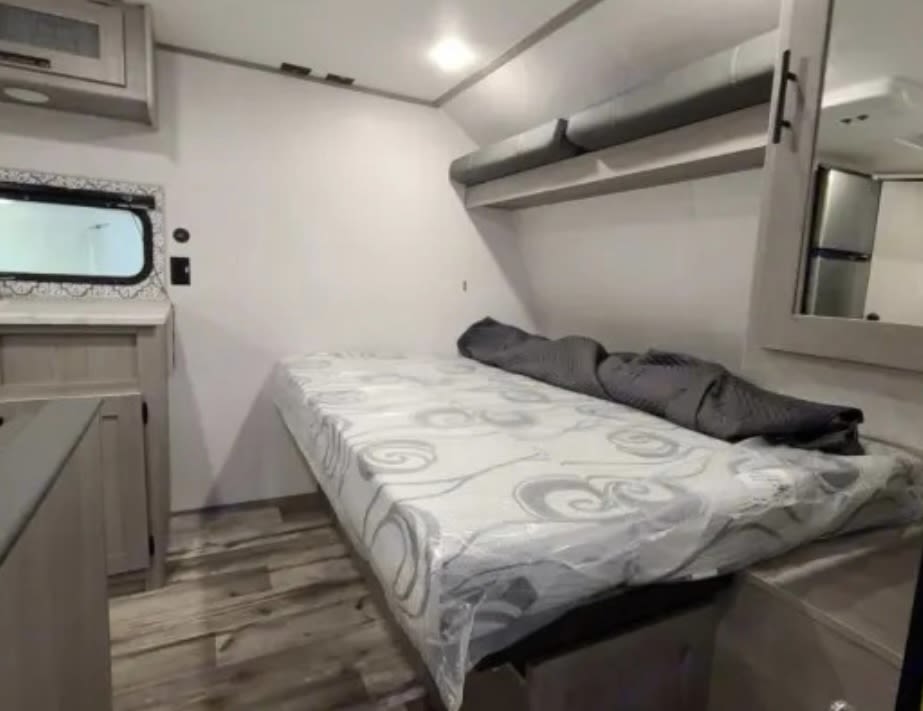 RV rental interior: cozy bedroom with bed, overhead bunk, and a compact living space featuring wood floors.. Dutchmen Coleman Lantern LT 2021