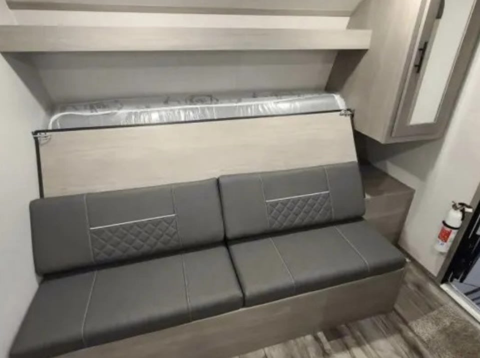 RV rental interior features grey dinette seating below an overhead bunk bed. Compact space with cabinet & fire extinguisher.. Dutchmen Coleman Lantern LT 2021