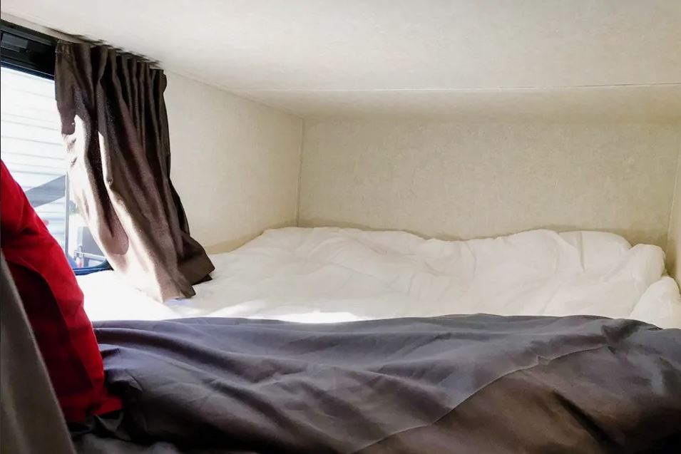 RV rental bunk bed view. Cozy interior with white & grey bedding, window with curtain. Ideal compact sleeping space.. Jayco Jay Flight 2020