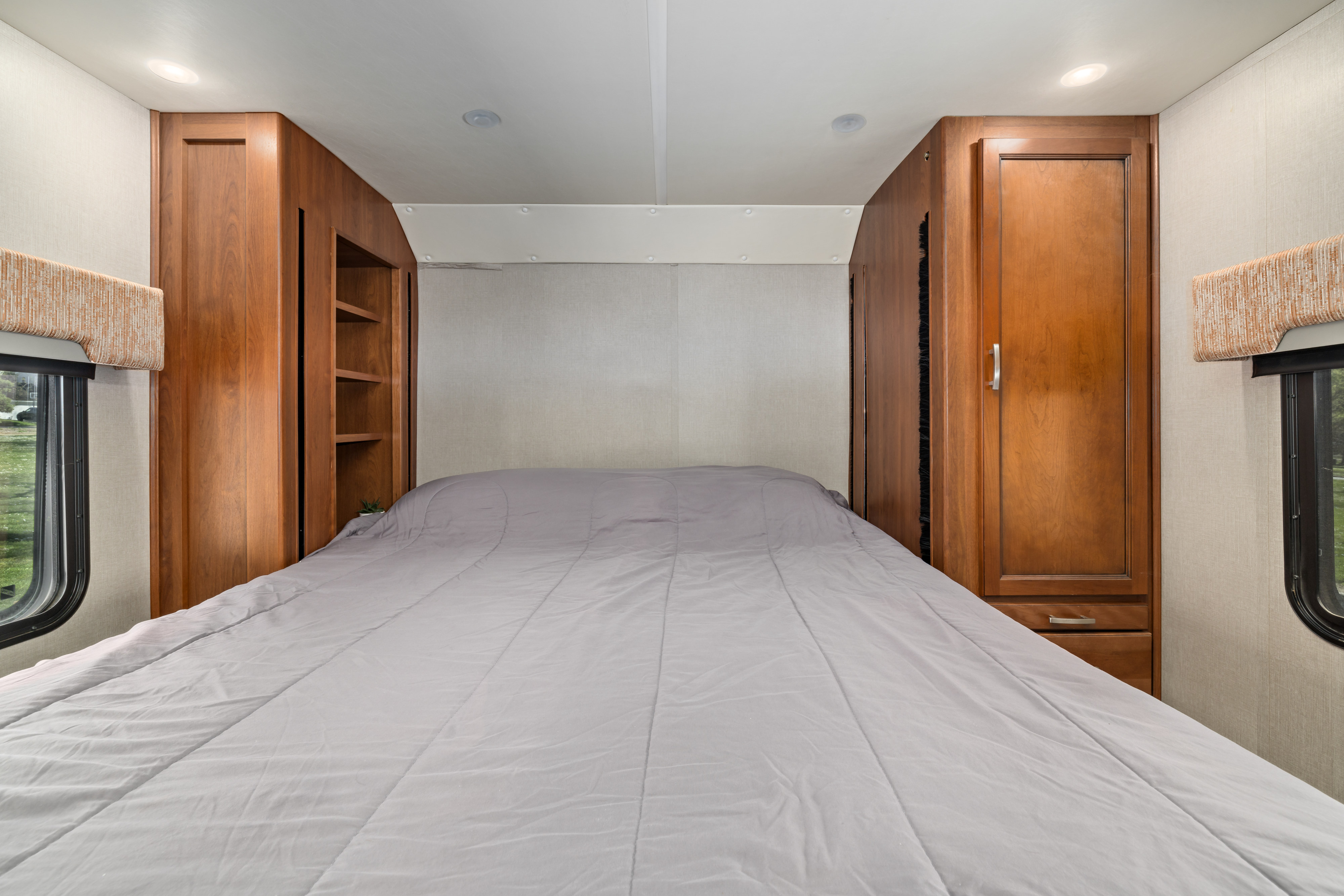 Compact RV rental bedroom with a comfy bed, built-in wooden storage, overhead lights, and side windows.. Monaco Trek 26HMD 2016