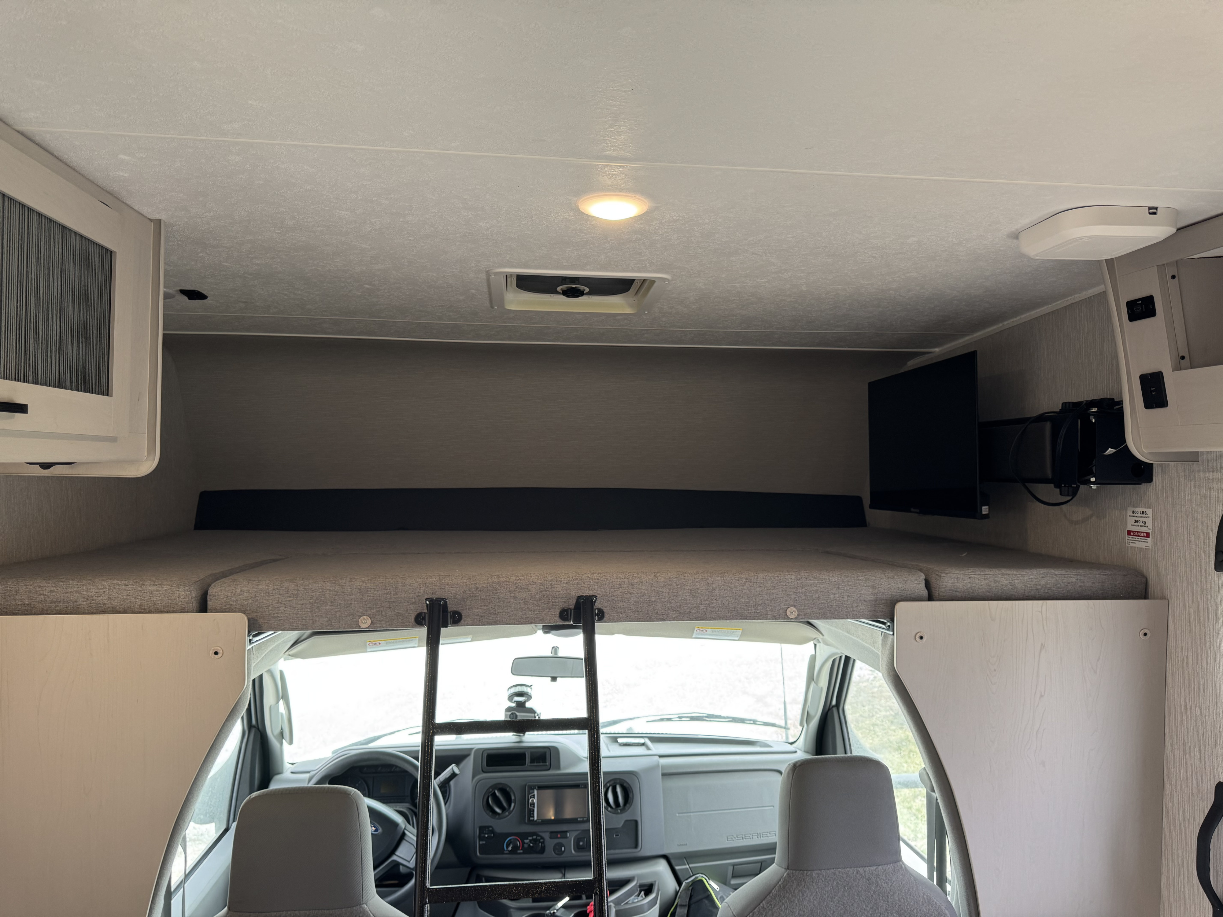 Inside an RV rental: view of the overhead bunk bed, ladder, and front cab from the living area.. Forest River Coachmen Freelander 2023