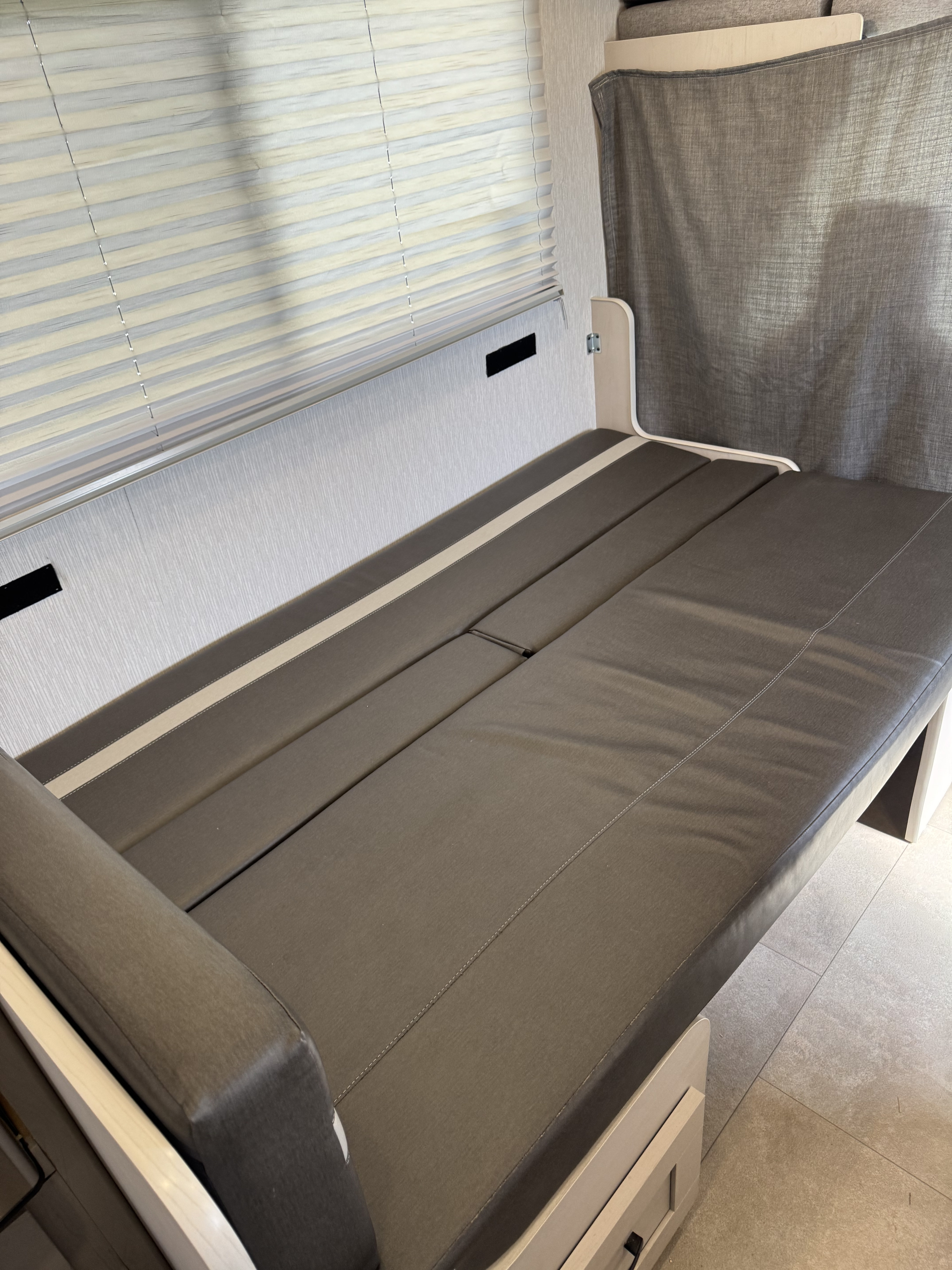 RV rental interior: Convertible gray upholstered seating/bed unit with window blinds and privacy curtain for comfort.. Forest River Coachmen Freelander 2023