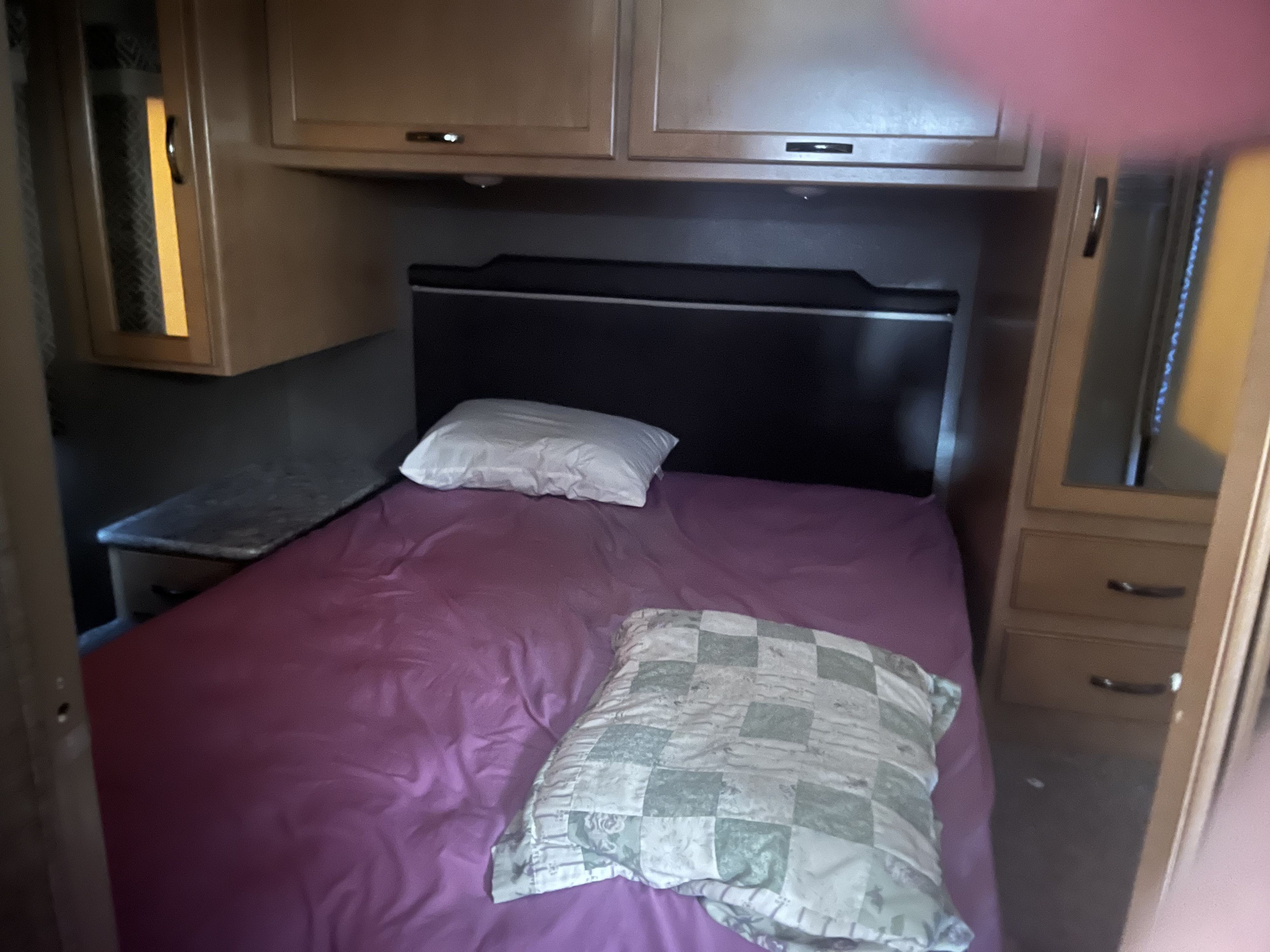 Cozy RV rental bedroom featuring a bed with purple bedding, headboard, and built-in wooden cabinets.. Thor Four Winds 2018