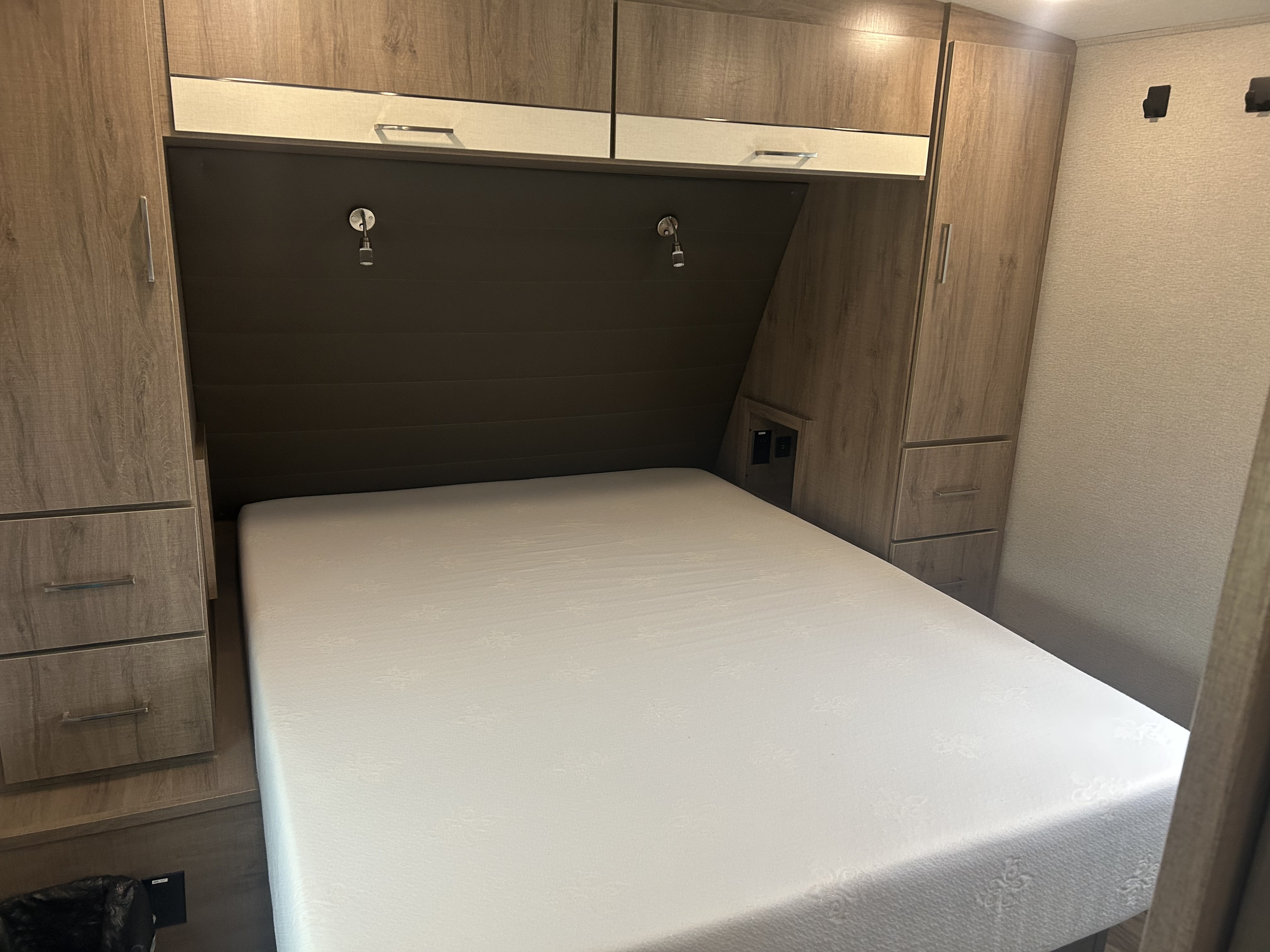 RV rental bedroom: a compact interior with a white mattress, overhead cabinets, built-in storage & reading lights.. Grand Design Imagine 2022