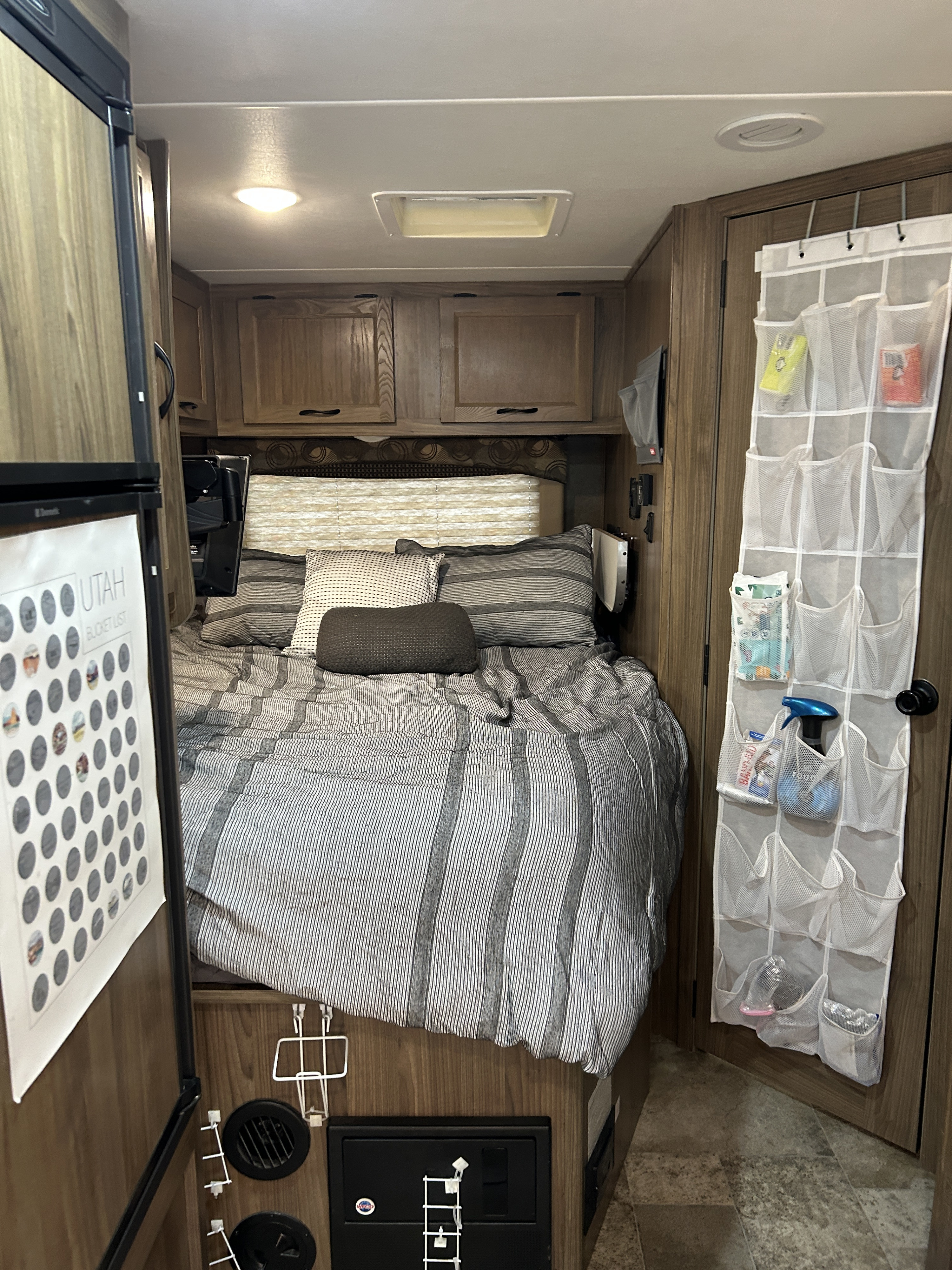 Cozy RV rental bedroom with striped bedding, overhead storage, and a practical hanging organizer on the door.. Forest River Coachmen Freelander 2017