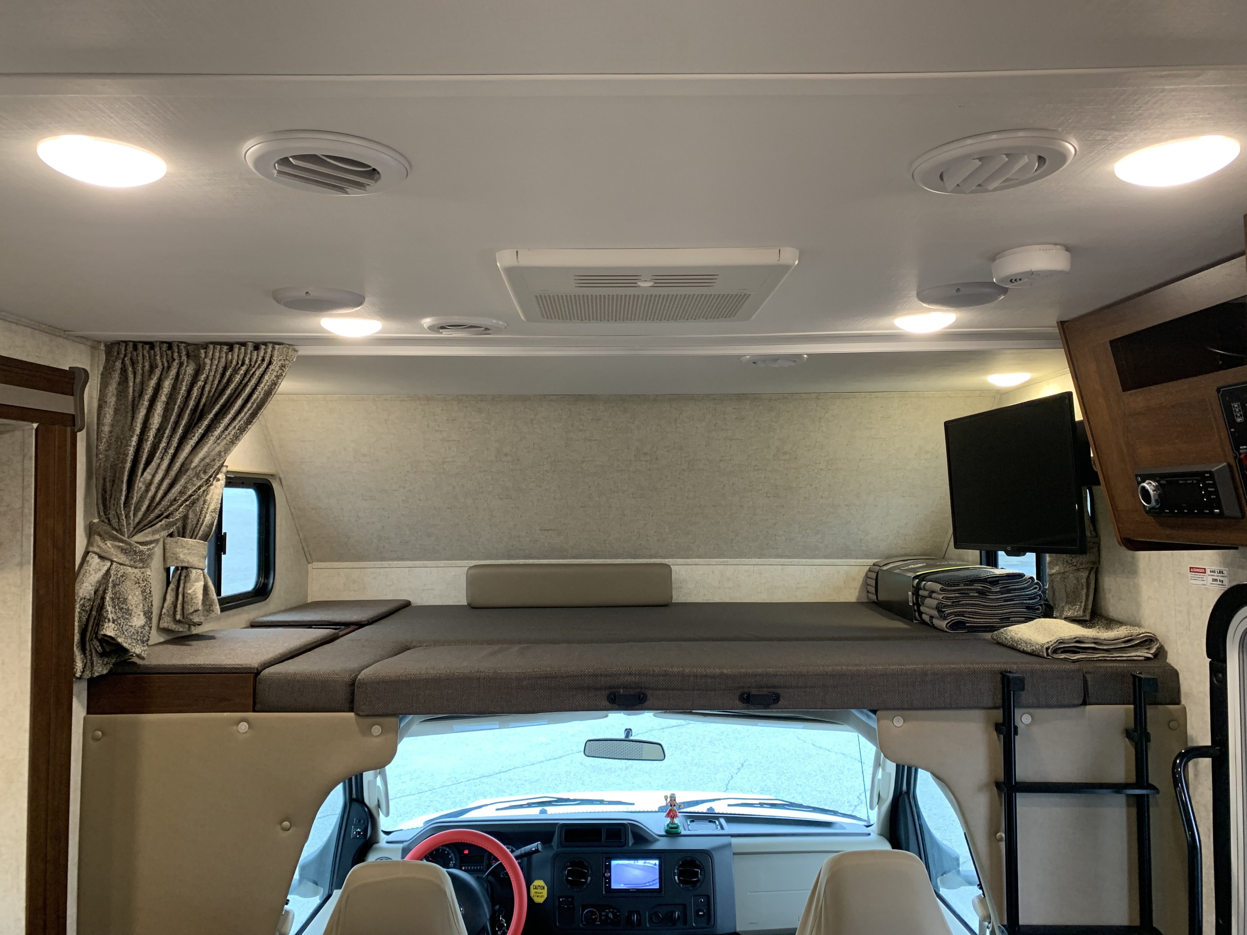 RV rental interior, showcasing an over-cab bunk, mounted TV, controls, and driver's area below.. Forester Forester Motorhome 2020