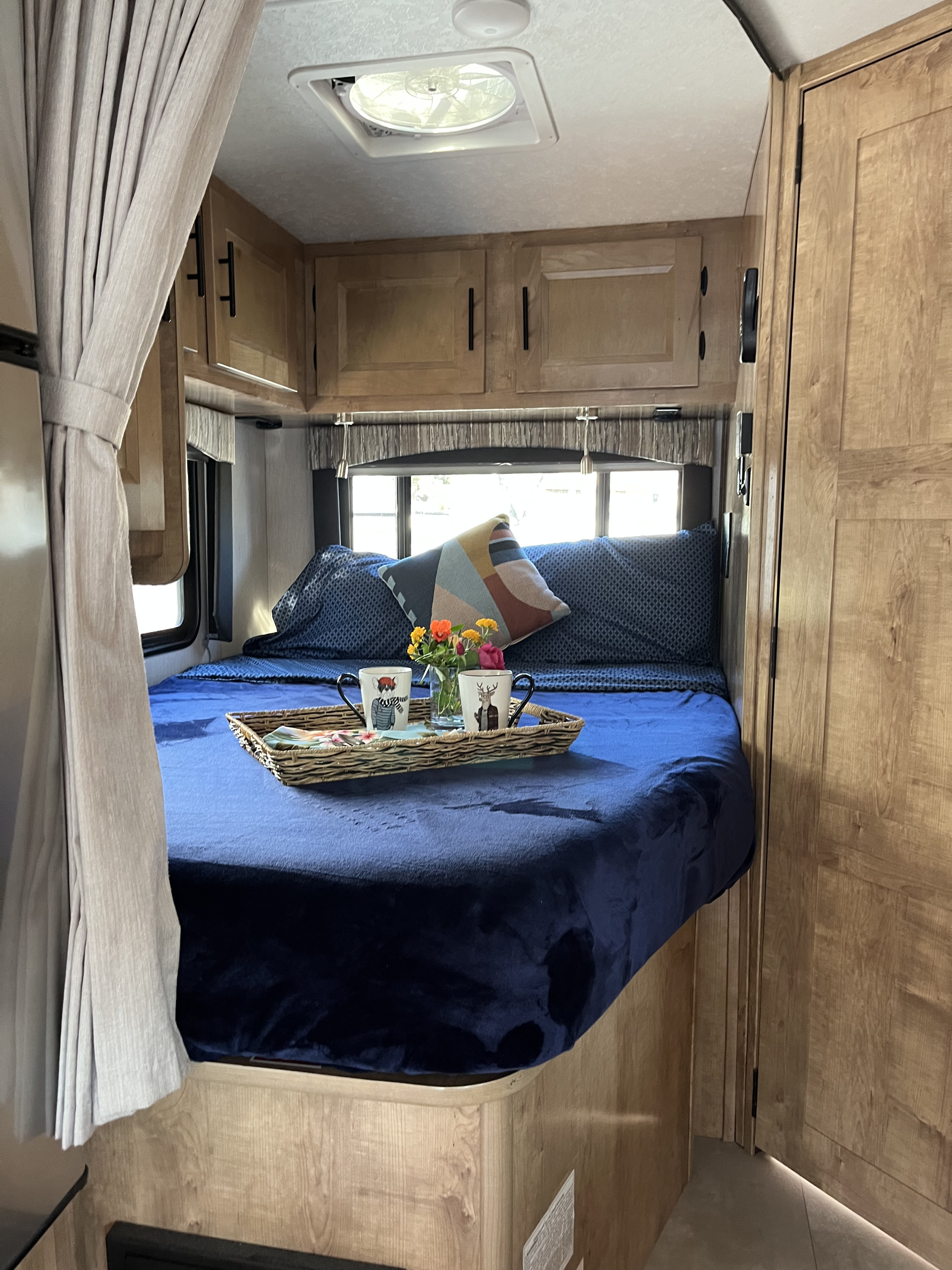 This cozy RV rental bedroom features a blue bed, decorative pillows, and a breakfast tray amidst warm wood cabinetry.. Coachmen Leprechaun 2021