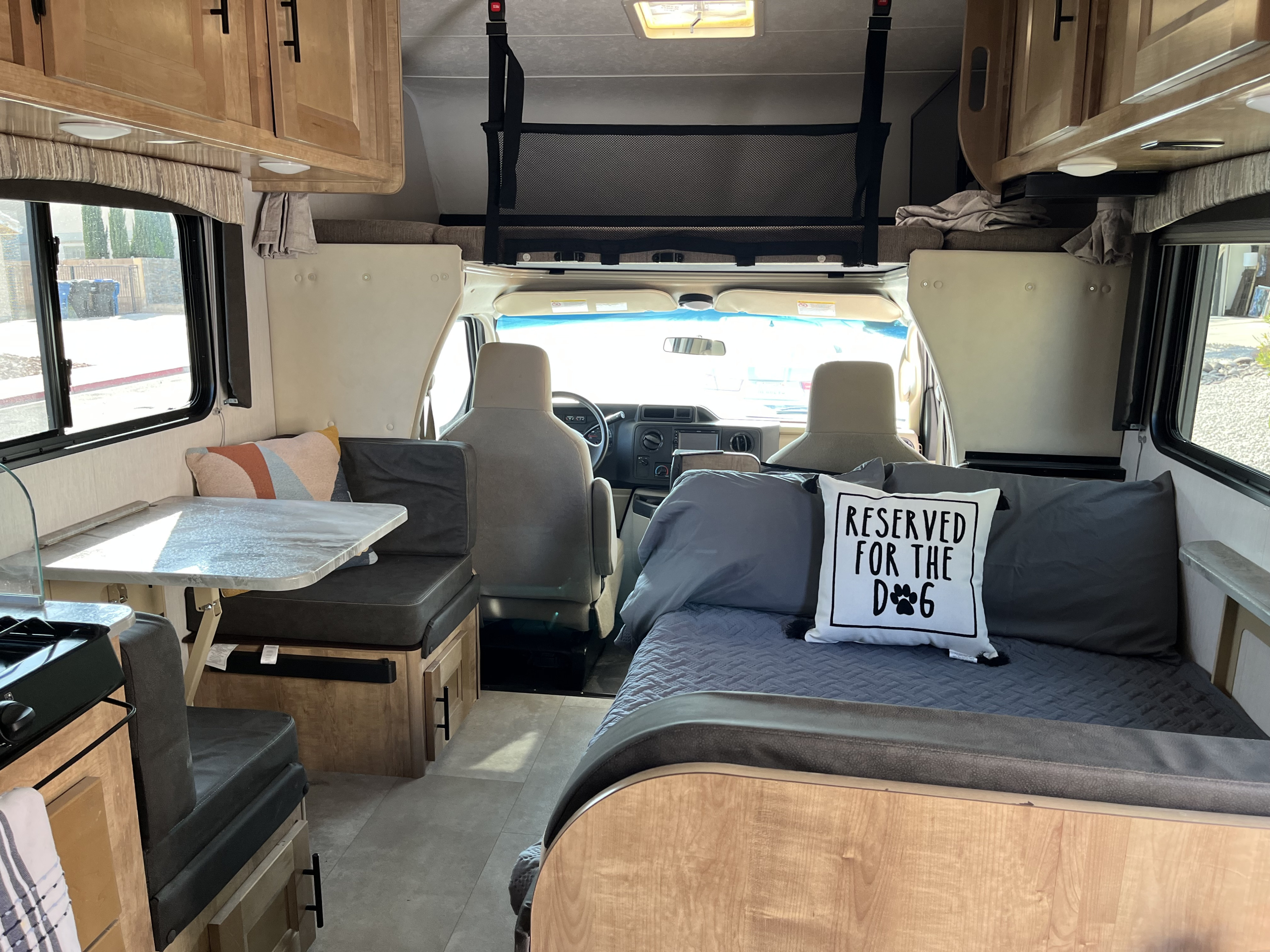 RV rental interior: bed with 'Reserved for the Dog' pillow, dinette, kitchen, and driver's area. Perfect for travel.. Coachmen Leprechaun 2021