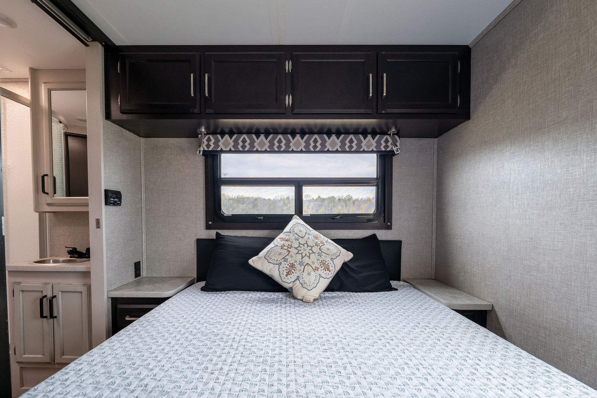 Modern RV rental bedroom: Features a comfy bed, overhead storage, window, and small vanity with sink.. Jayco Redhawk 2022