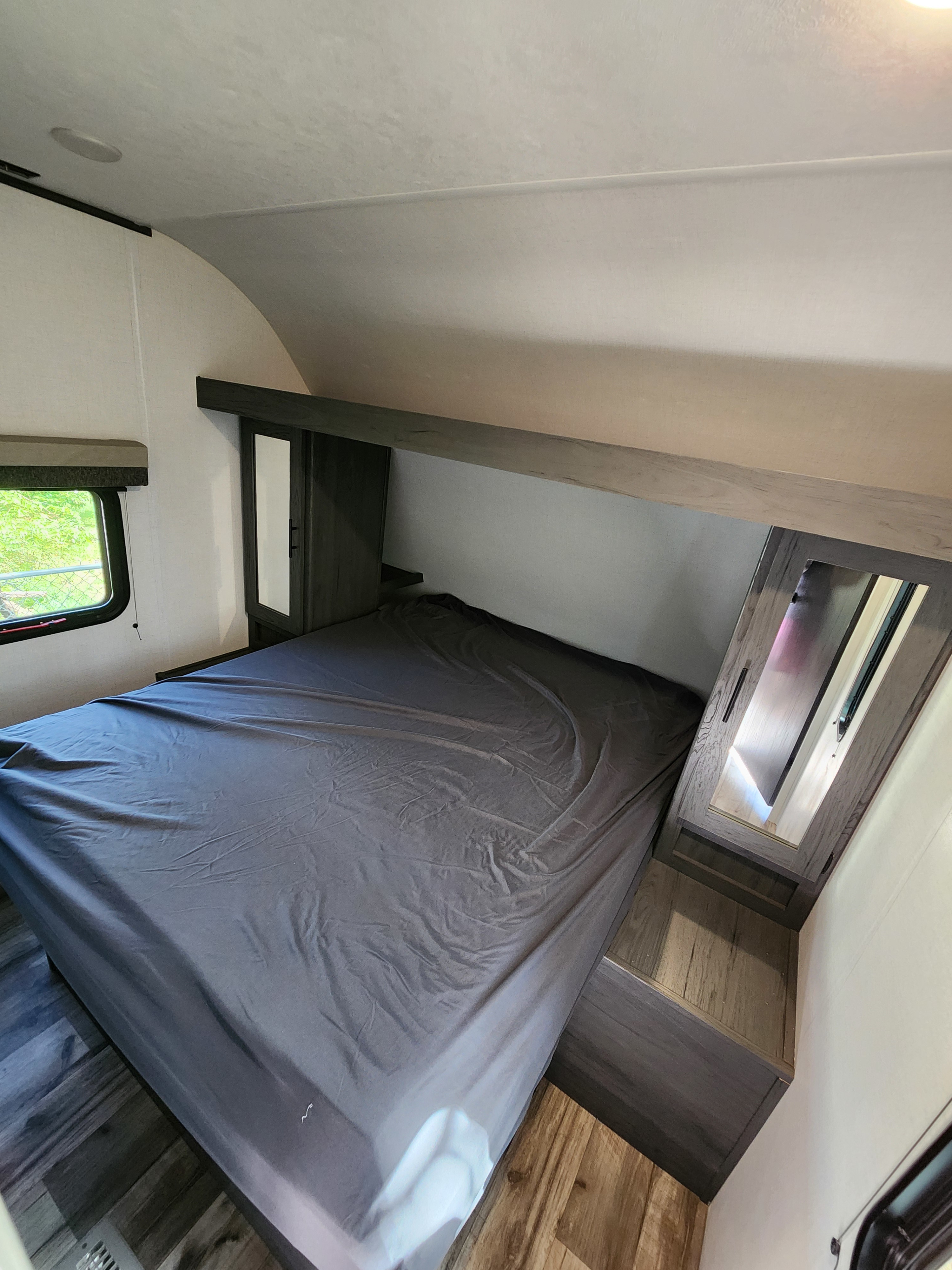 Experience comfort in this RV rental bedroom, featuring a cozy bed, mirrored cabinets, and window views for a relaxing stay.. Dutchmen Aspen Trail 26BH 2025