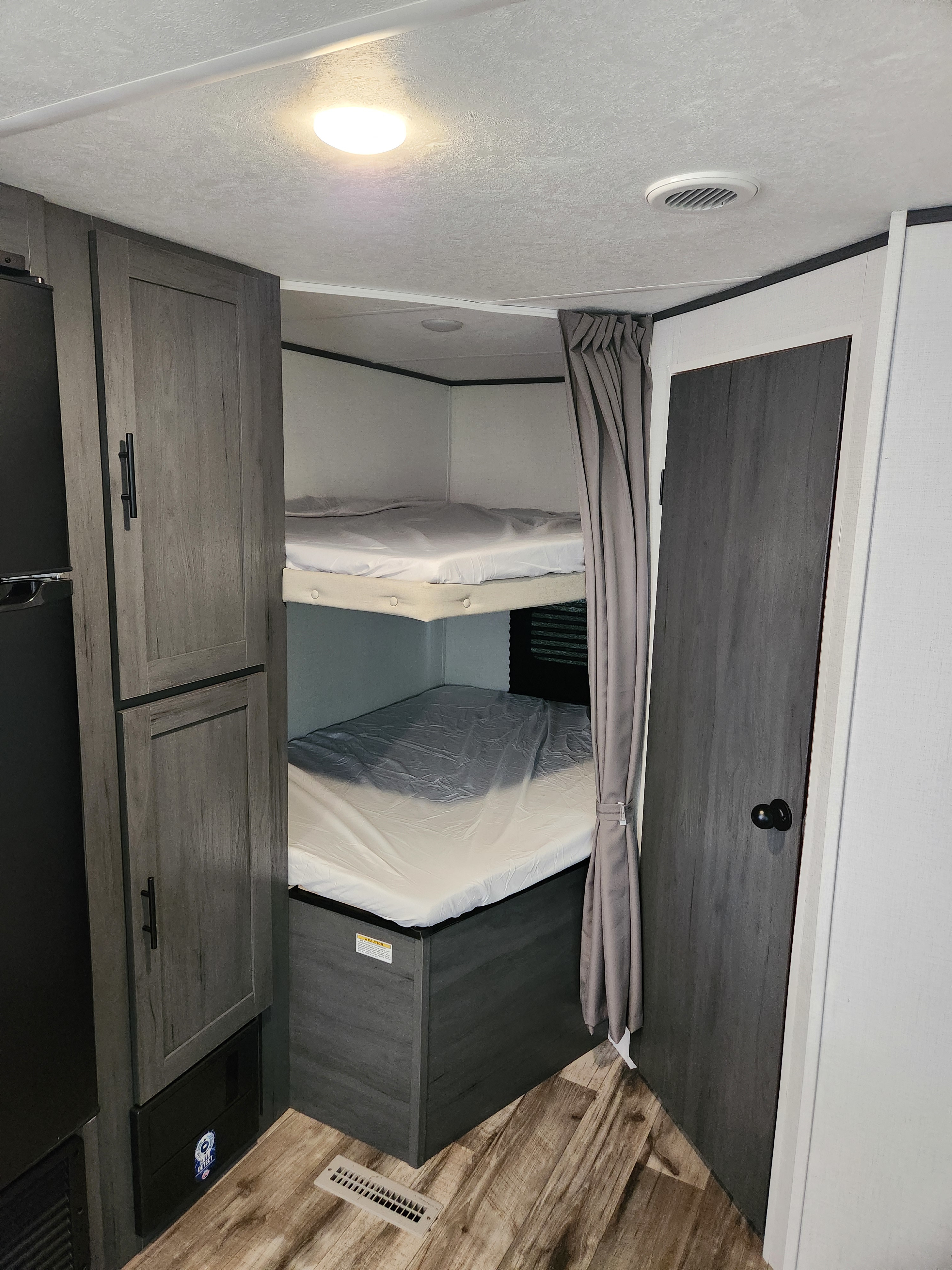 Cozy RV rental interior with two bunk beds and storage. This sleeping area features gray decor, a ceiling light, and wood flooring.. Dutchmen Aspen Trail 26BH 2025