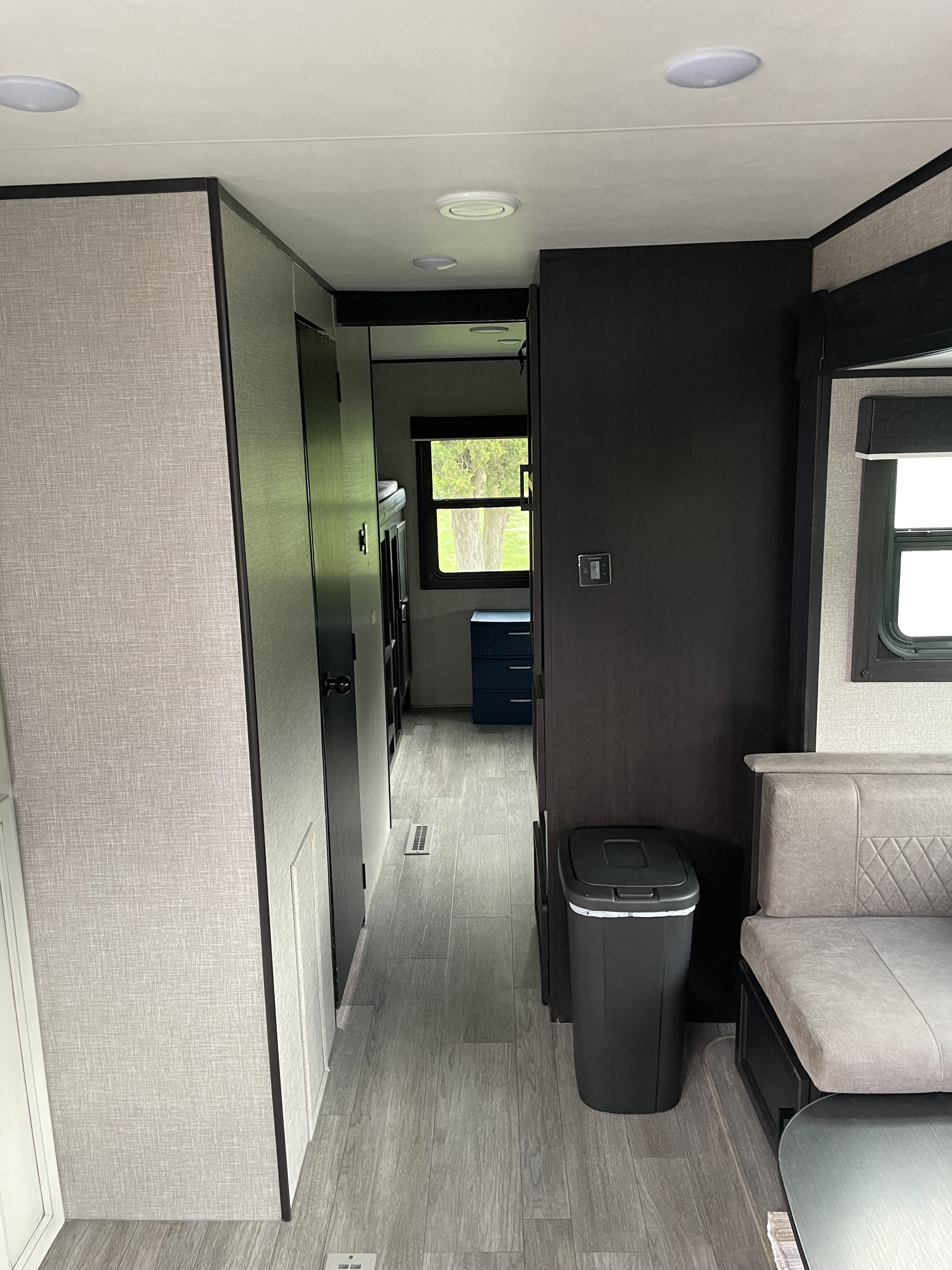Clean rv rental interior. Modern hallway with grey wood-look flooring, light walls, dark cabinetry, seating, and a view to the bunkhouse.. Jayco Jay Flight 2022