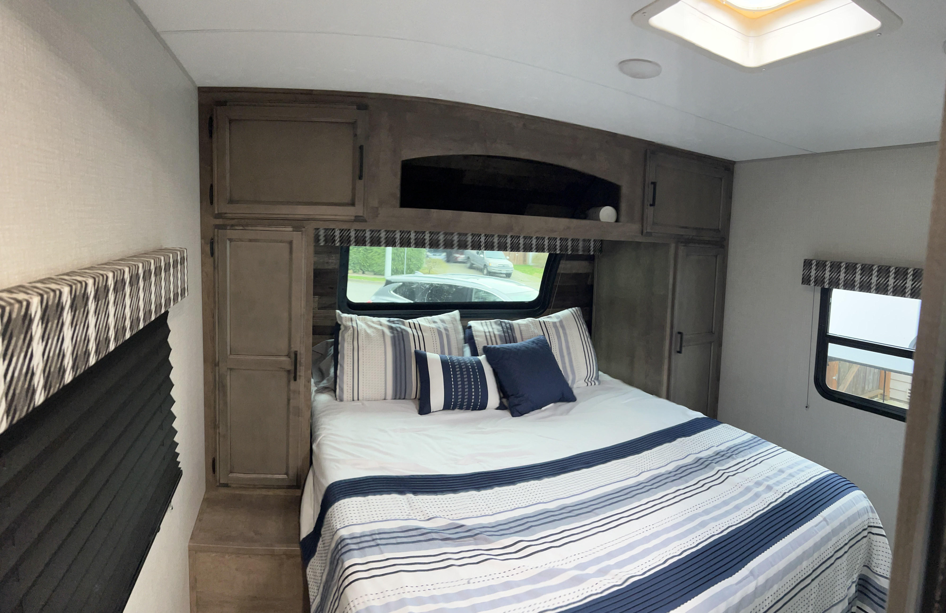 Cozy RV rental bedroom showcasing a bed with blue and white striped bedding, overhead storage, and natural light.. Venture Stratus 2021
