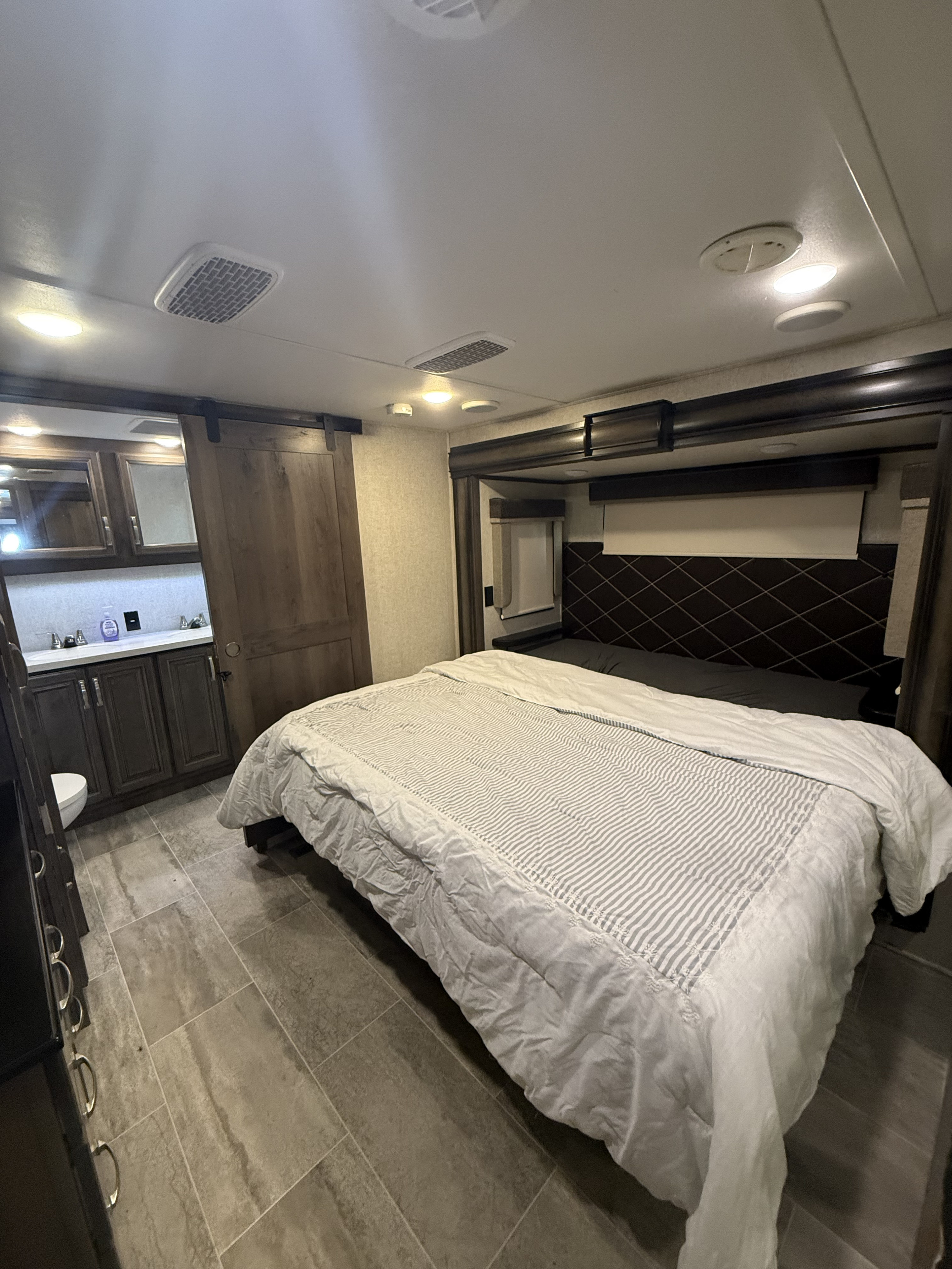 Spacious RV rental bedroom with modern bed, adjoining bathroom, and tiled floor for comfortable travels.. Keystone RV Montana 20th Anniversary 2019