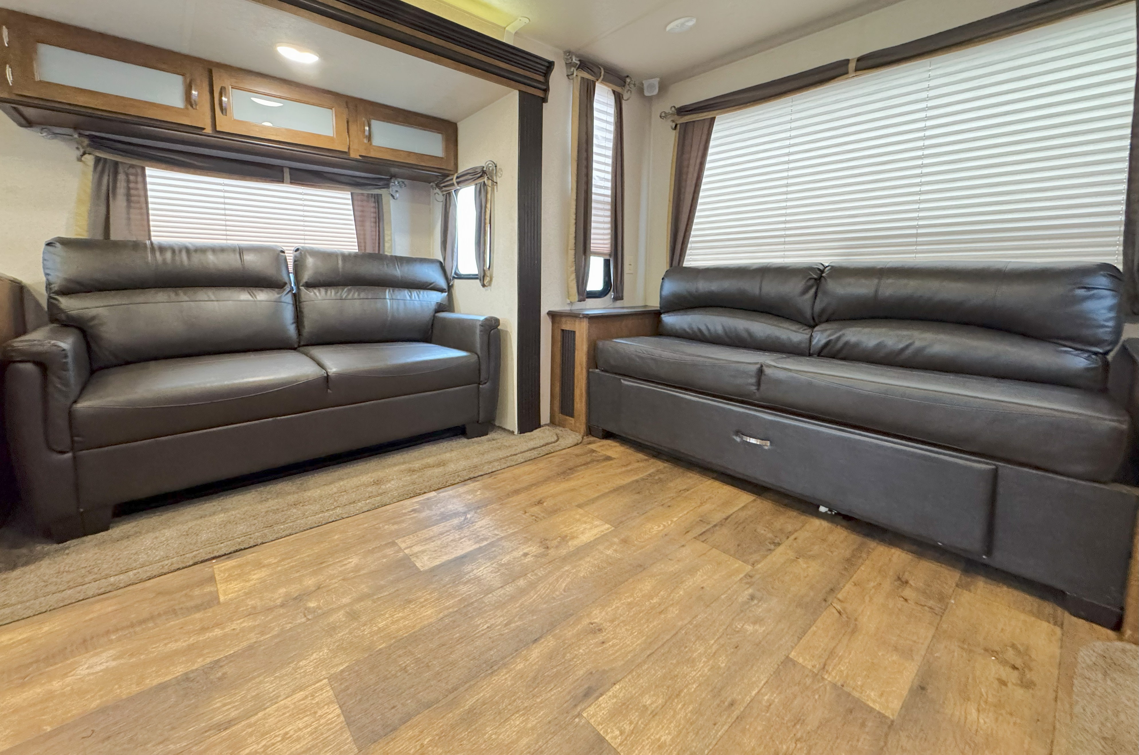 RV rental interior: spacious living area with two dark brown sofas, wood flooring, windows, and overhead cabinets.. Forest River Salem 2018