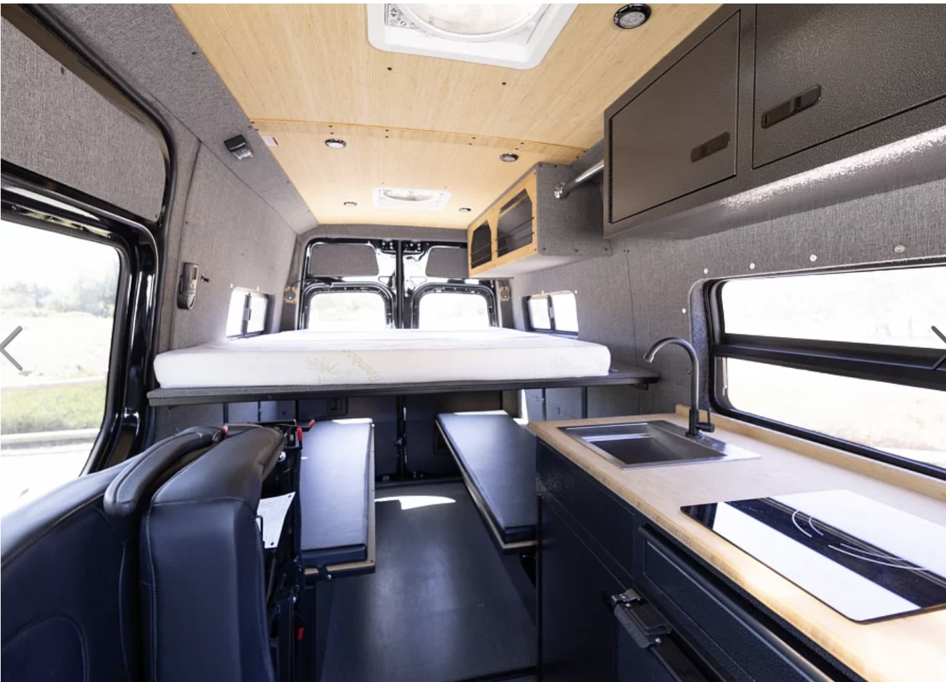 Modern rv rental interior with an elevated bed, compact kitchen, and convertible seating, perfect for adventures.. Mercedes-Benz Vanworks 2022