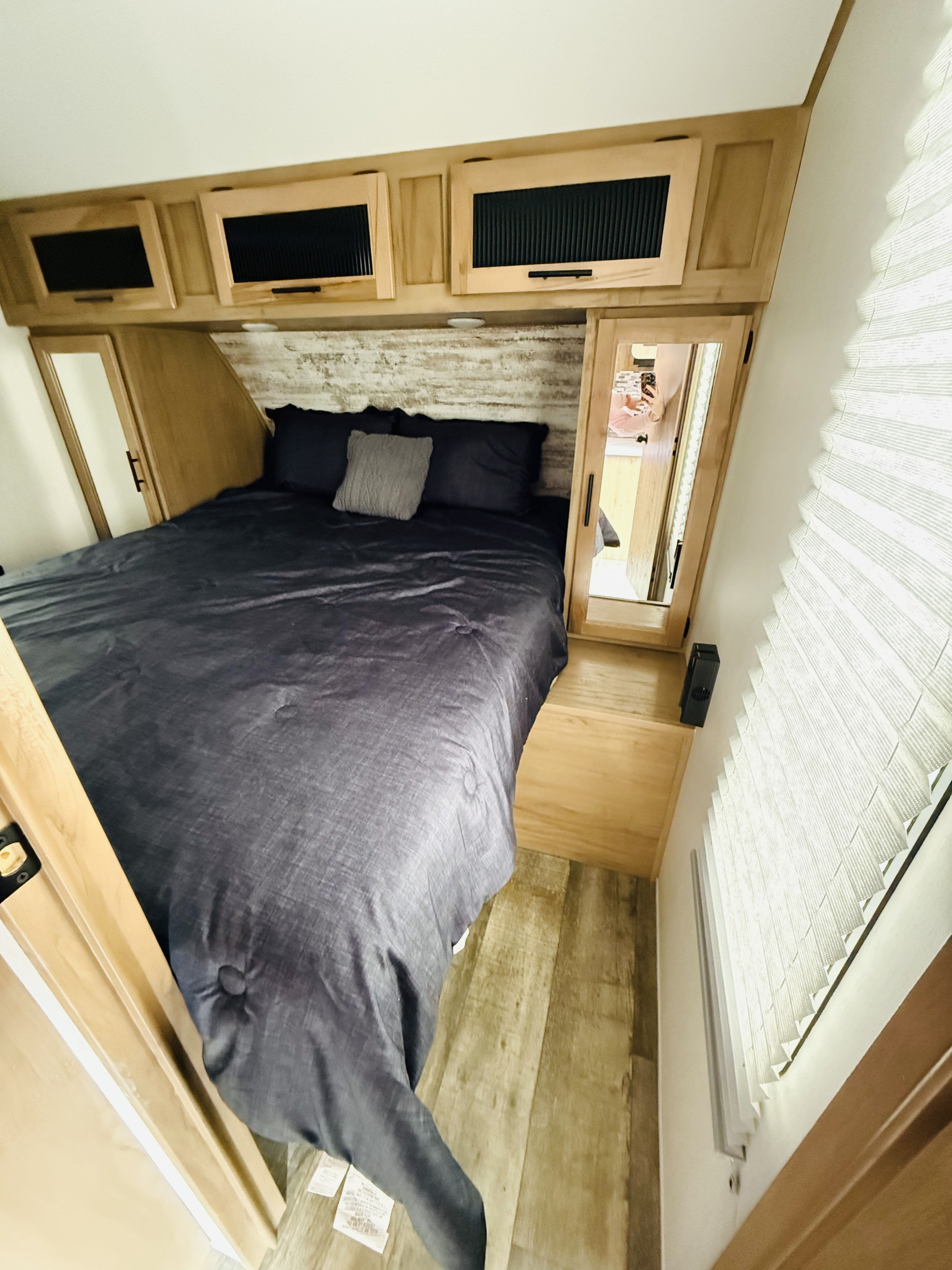 Cozy RV rental bedroom featuring a bed with dark gray bedding, overhead storage, and wood-look flooring and headboard.. Forest River Cherokee Alpha Wolf 2023
