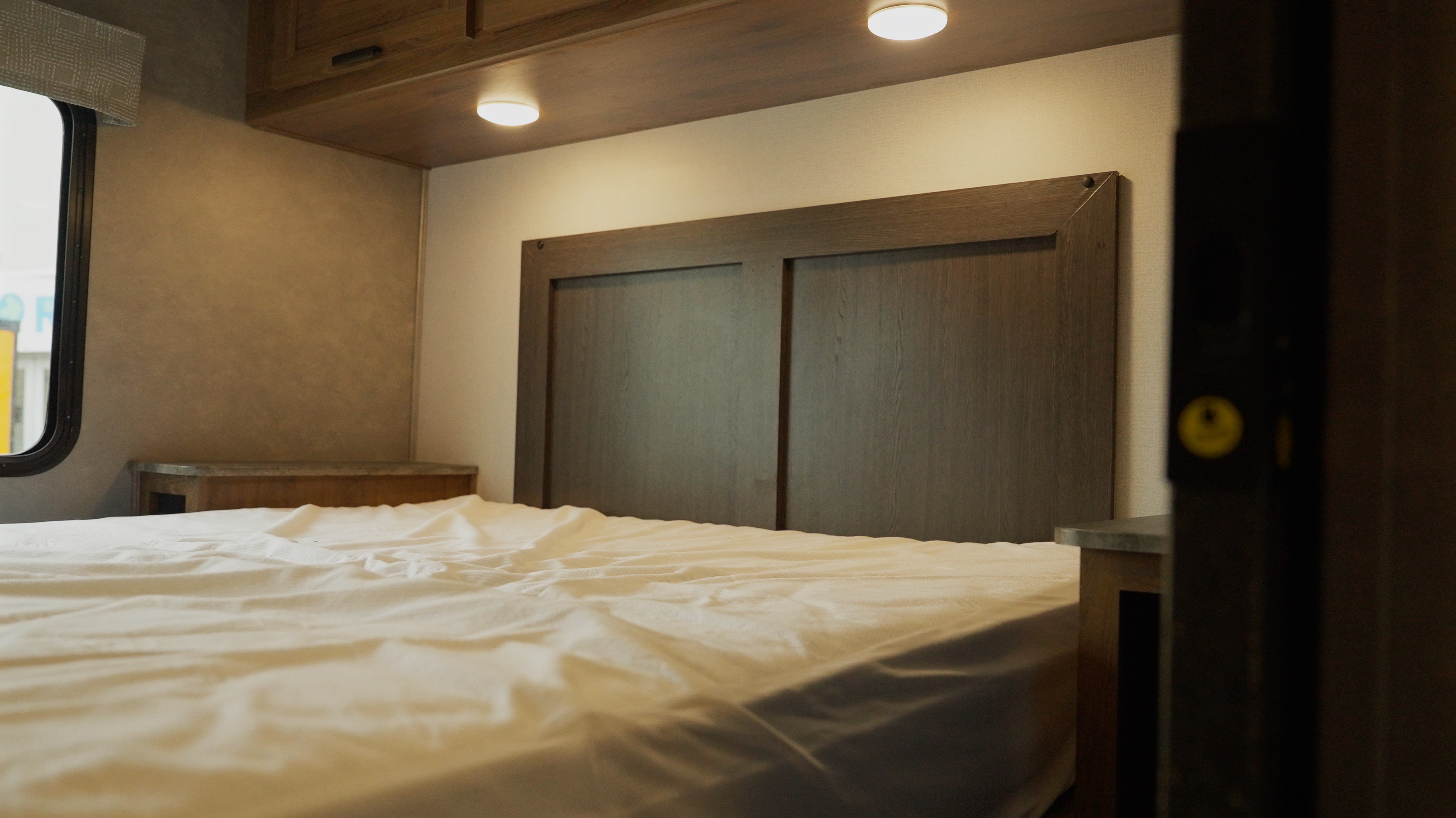 Cozy RV rental bedroom with a comfy bed, modern headboard, overhead cabinets & lights, perfect for travel.. Forest River Sunseeker 2024