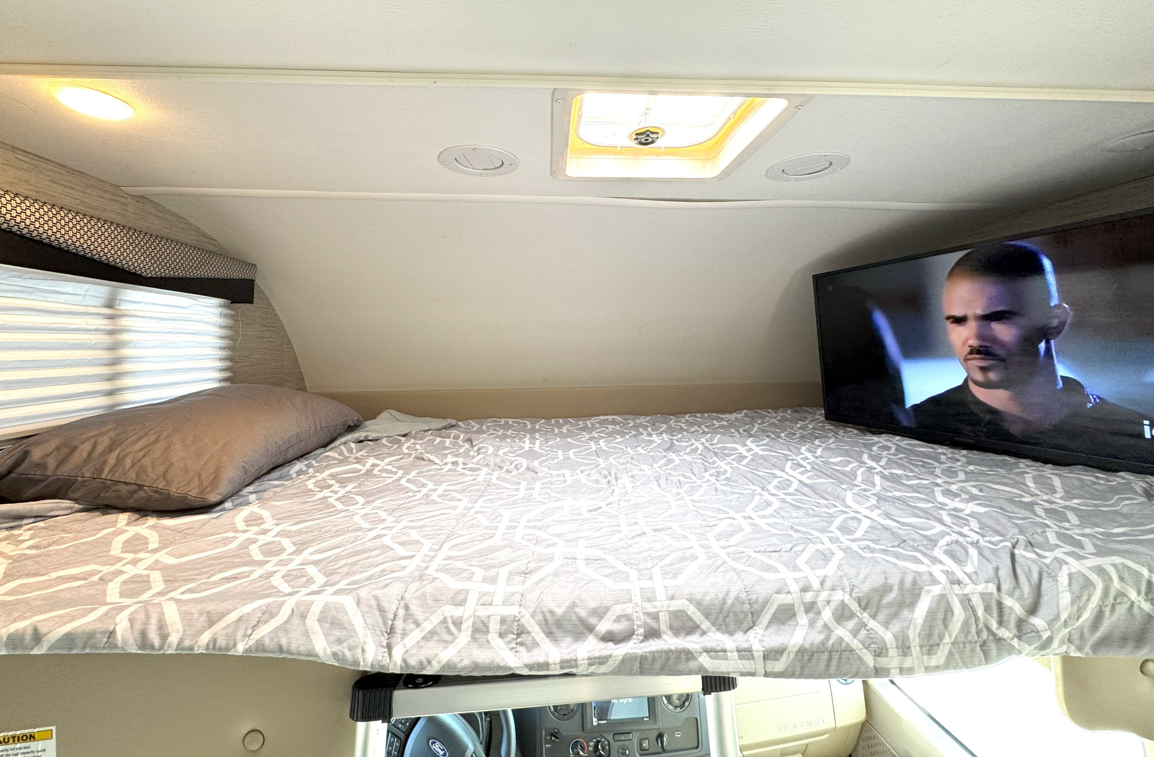 RV rental's cozy cab-over bunk bed, with a patterned comforter and TV, ready for your motorhome adventure.. Thor Motor Coach Freedom Elite 2023