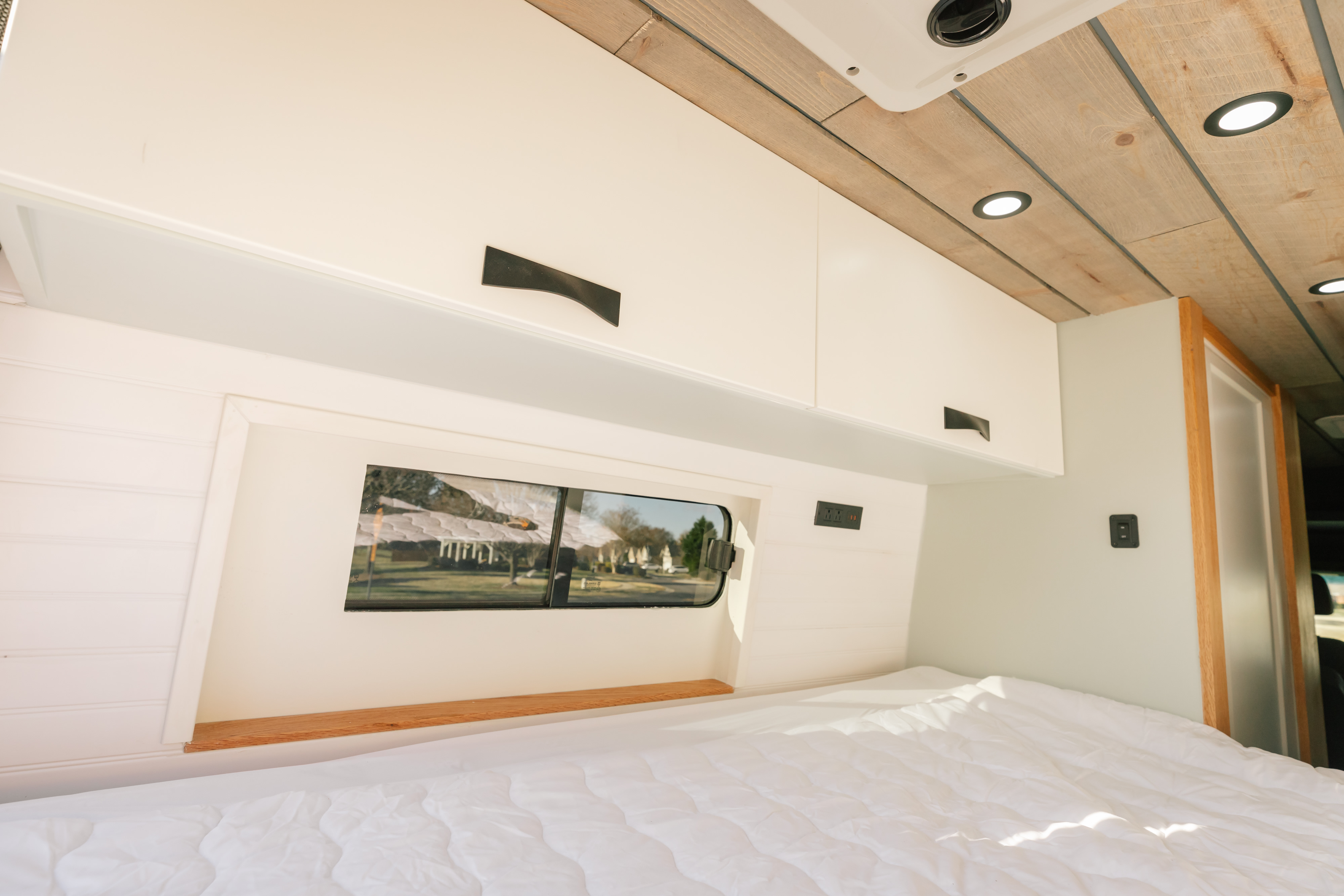 Bright RV rental bedroom features a cozy bed, overhead cabinets, and a window for scenic views.. Sovereign Vans Mercedes Benz Sprinter 2500 4*4 2024