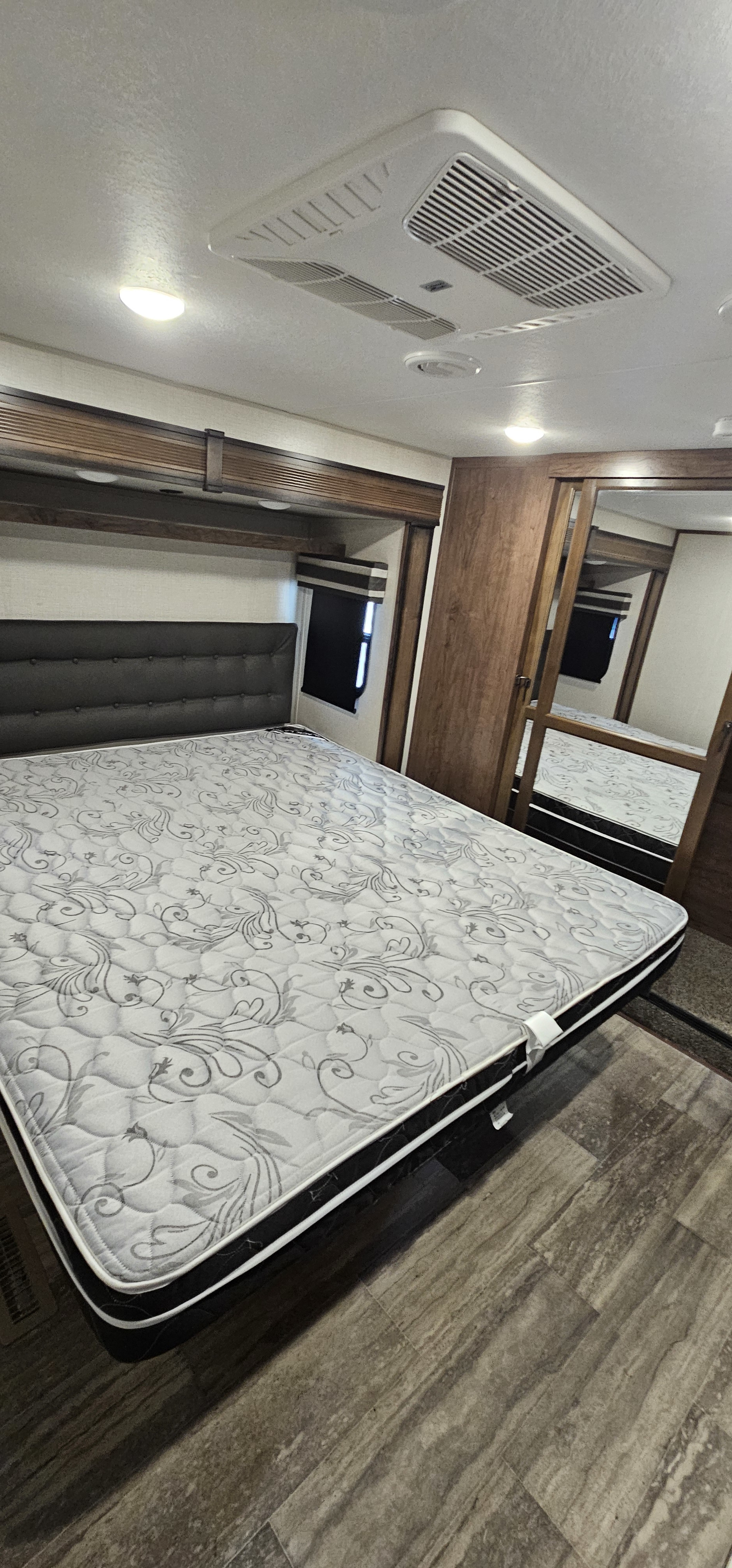 Clean RV rental bedroom with a large bed, decorative mattress, AC unit, and mirrored wardrobe for your travel comfort.. K-Z Manufacturing Durango 2021