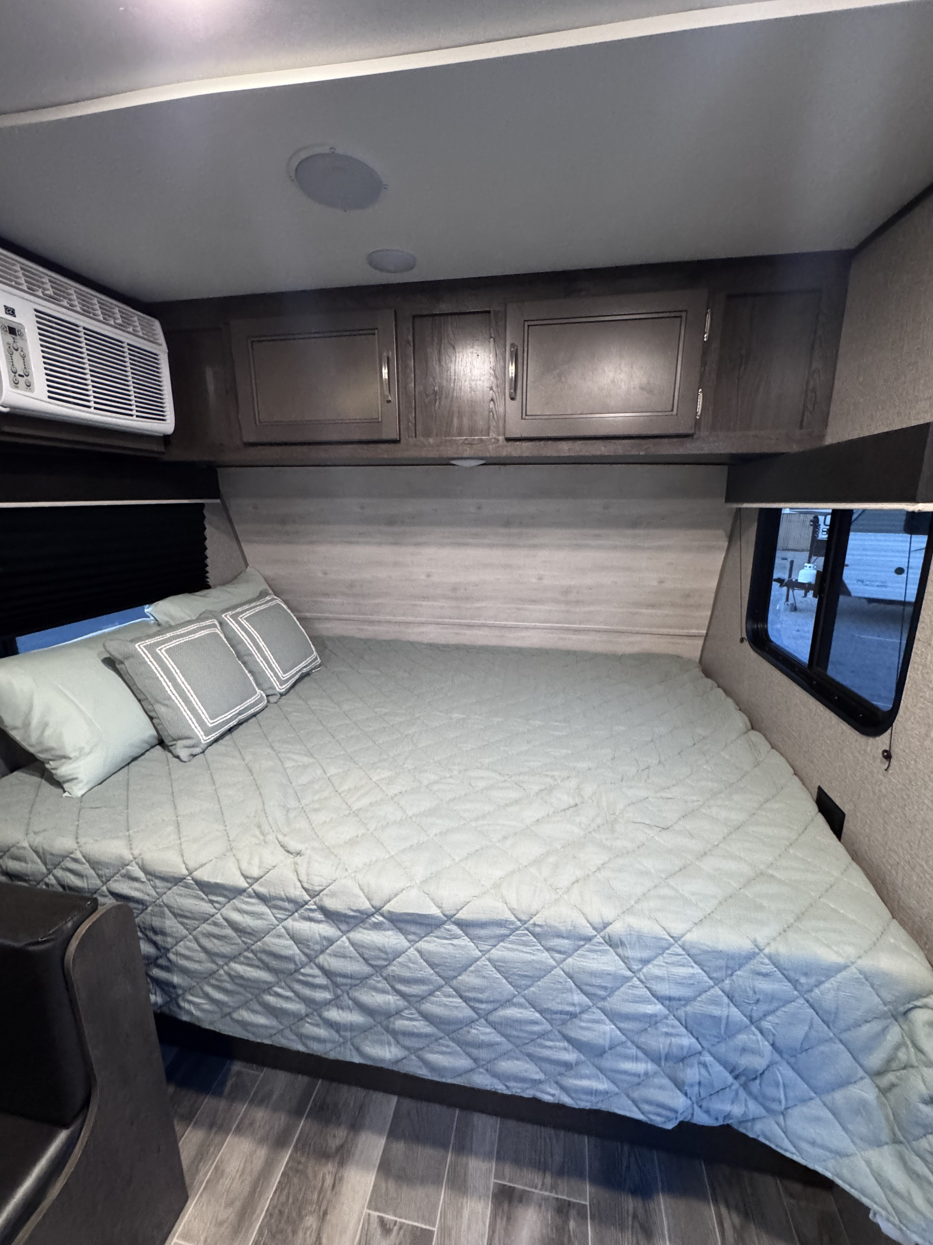 Cozy RV rental bedroom with a large bed, overhead cabinets, window AC, and outside view, offering compact comfort.. Jayco Jay Flight SLX Baja Edition 2021
