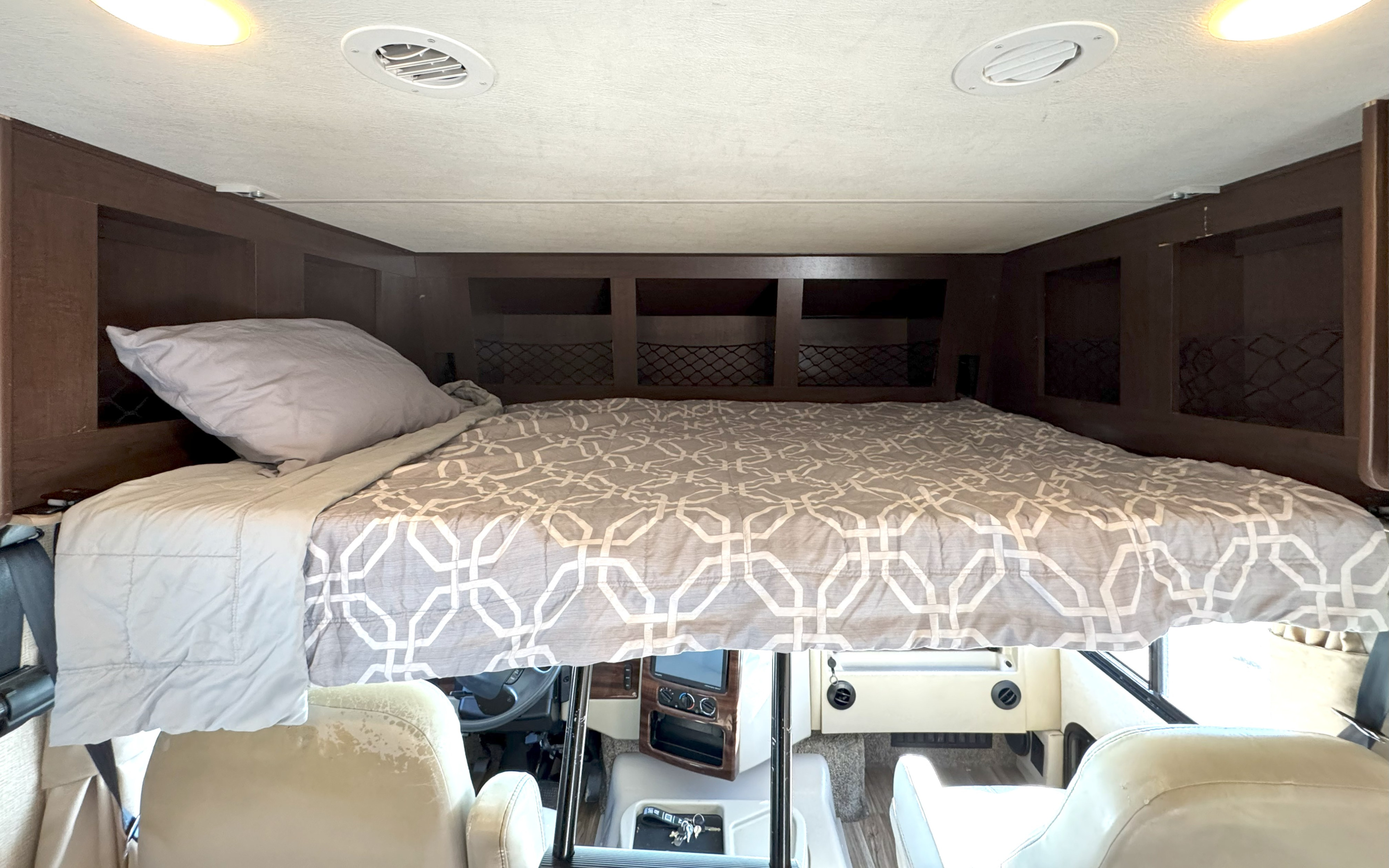 Overhead bunk bed in an RV rental, featuring bedding, storage, and visible cockpit area below.. Thor Motor Coach A.C.E 2019