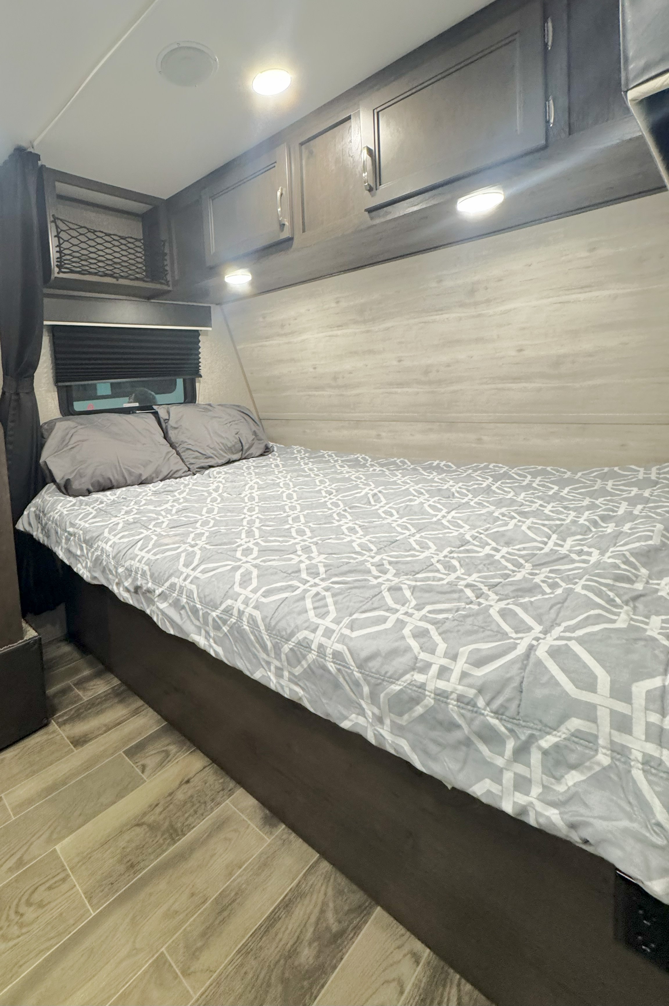 Cozy RV rental bedroom featuring a comfy bed with patterned quilt, overhead cabinets, and wood-look flooring.. Jayco Jay Flight SLX7 184BS 2021
